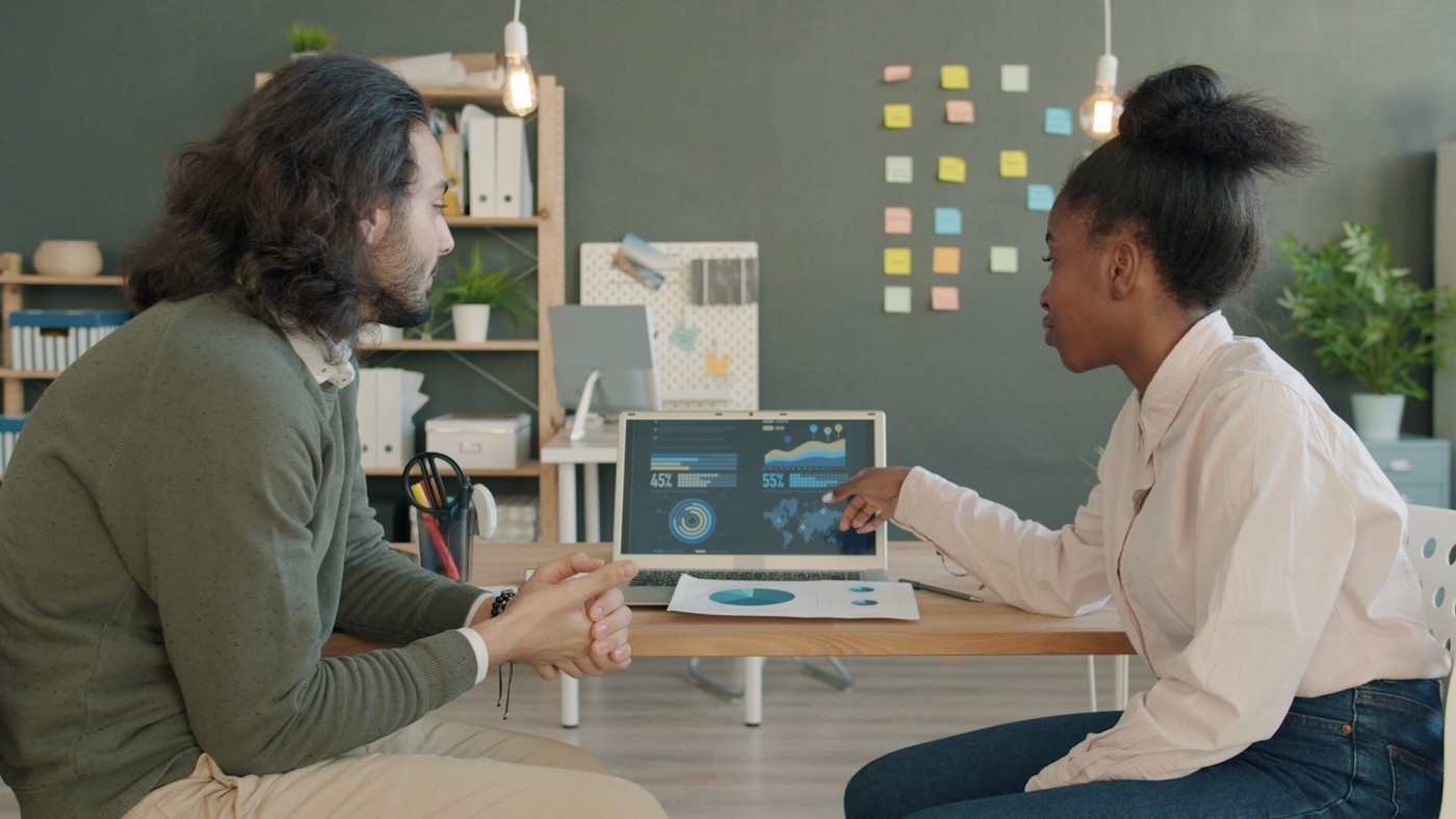 Two colleagues discussing data on a laptop screen