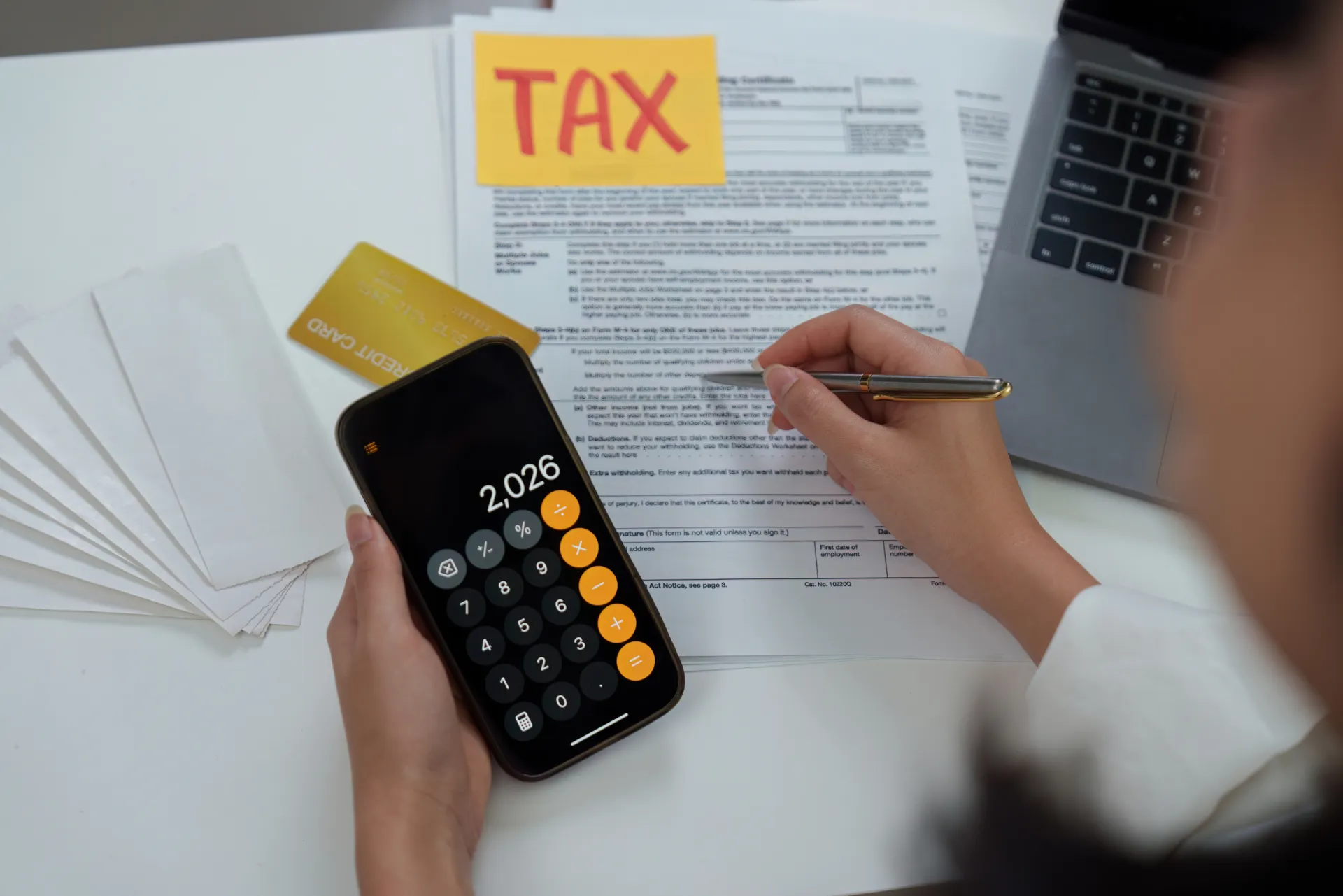 Jemand der gerade seine Steuererklärung macht und in der Hand ein Handy mit dem Taschenrechner hat auf dem "2026" eingetippt wurde.