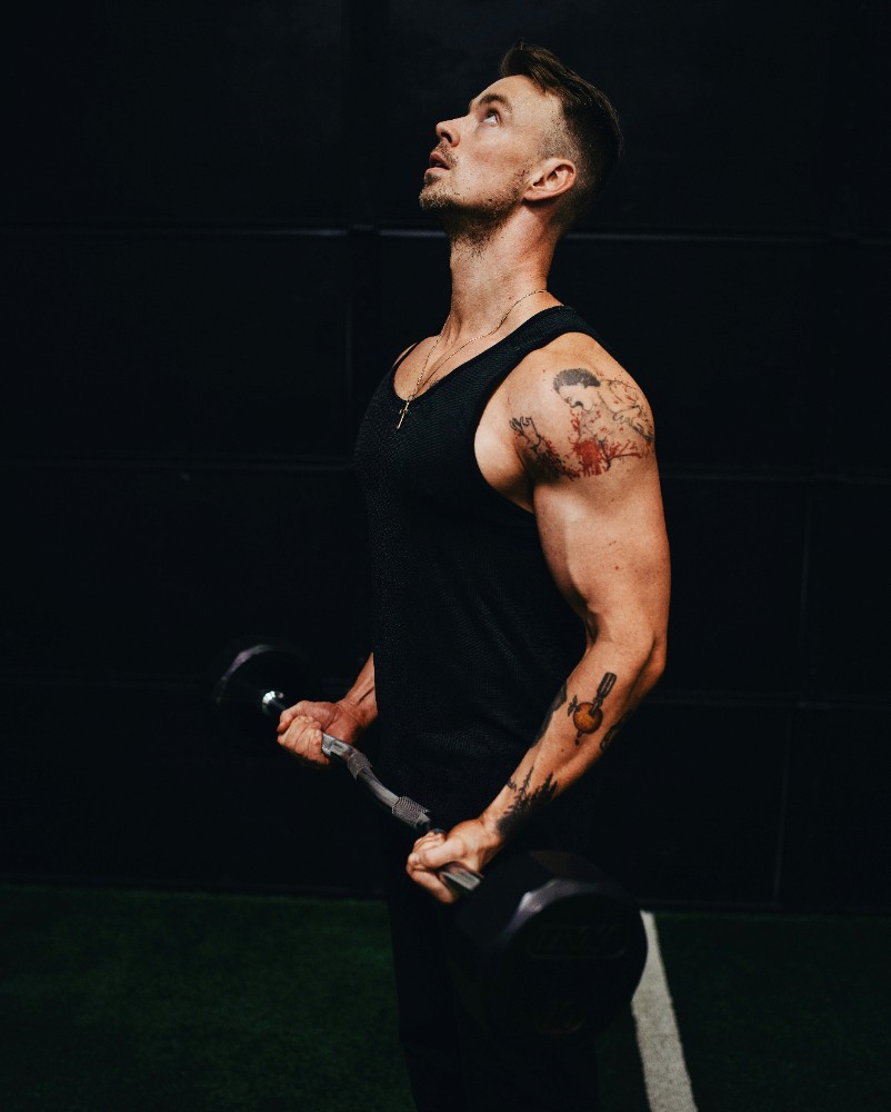 A muscular man lifting a dumbbell and looking upward with a focused expression. Quote below reads: “I’ve never felt this strong and confident in my life…” – Samantha Lee, Marketing Director.
