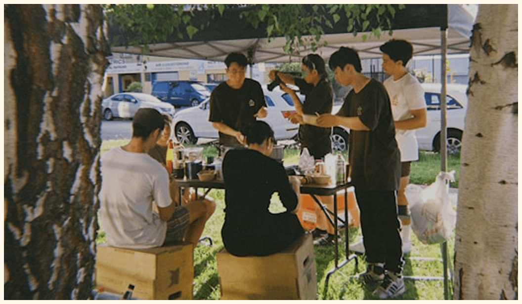 Group sharing food under canopy in grassy urban area
