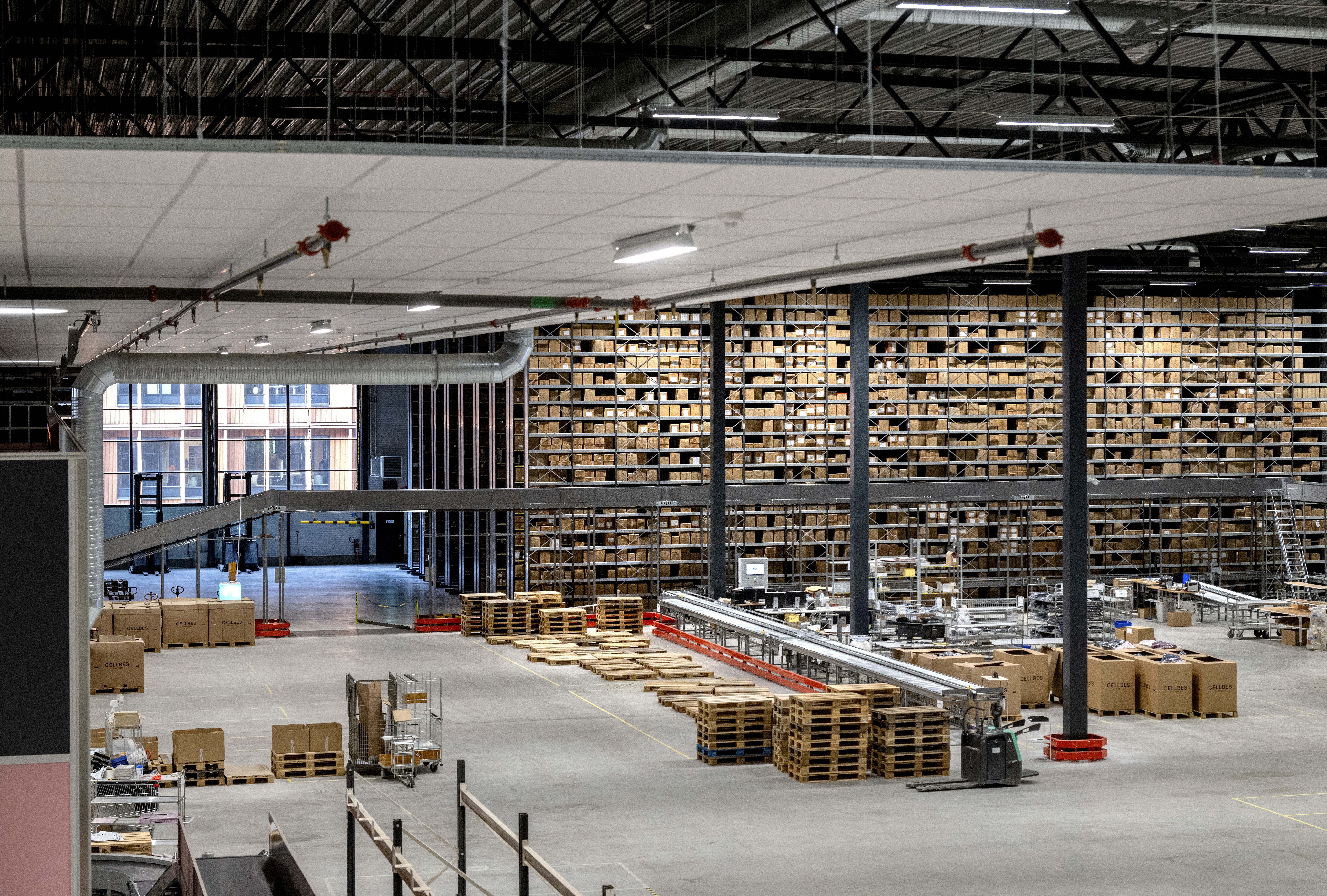 En stor lagerlokal fylld med pallar och kartonger, med transportband och lastutrymmen.