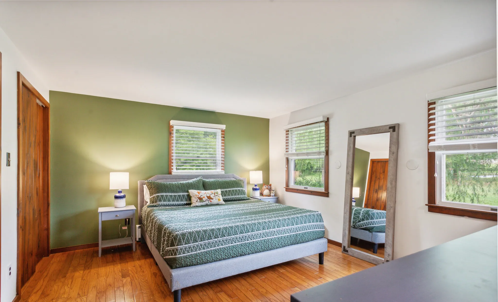 Main floor king bedroom with teal bedding, mirror and hardwood floors at Rocking Horse Acres