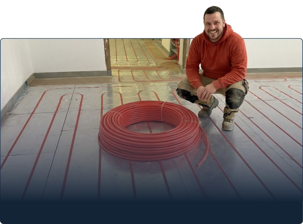 Ein Mann verlegt Wasserrohre einer Fußbodenheizung.