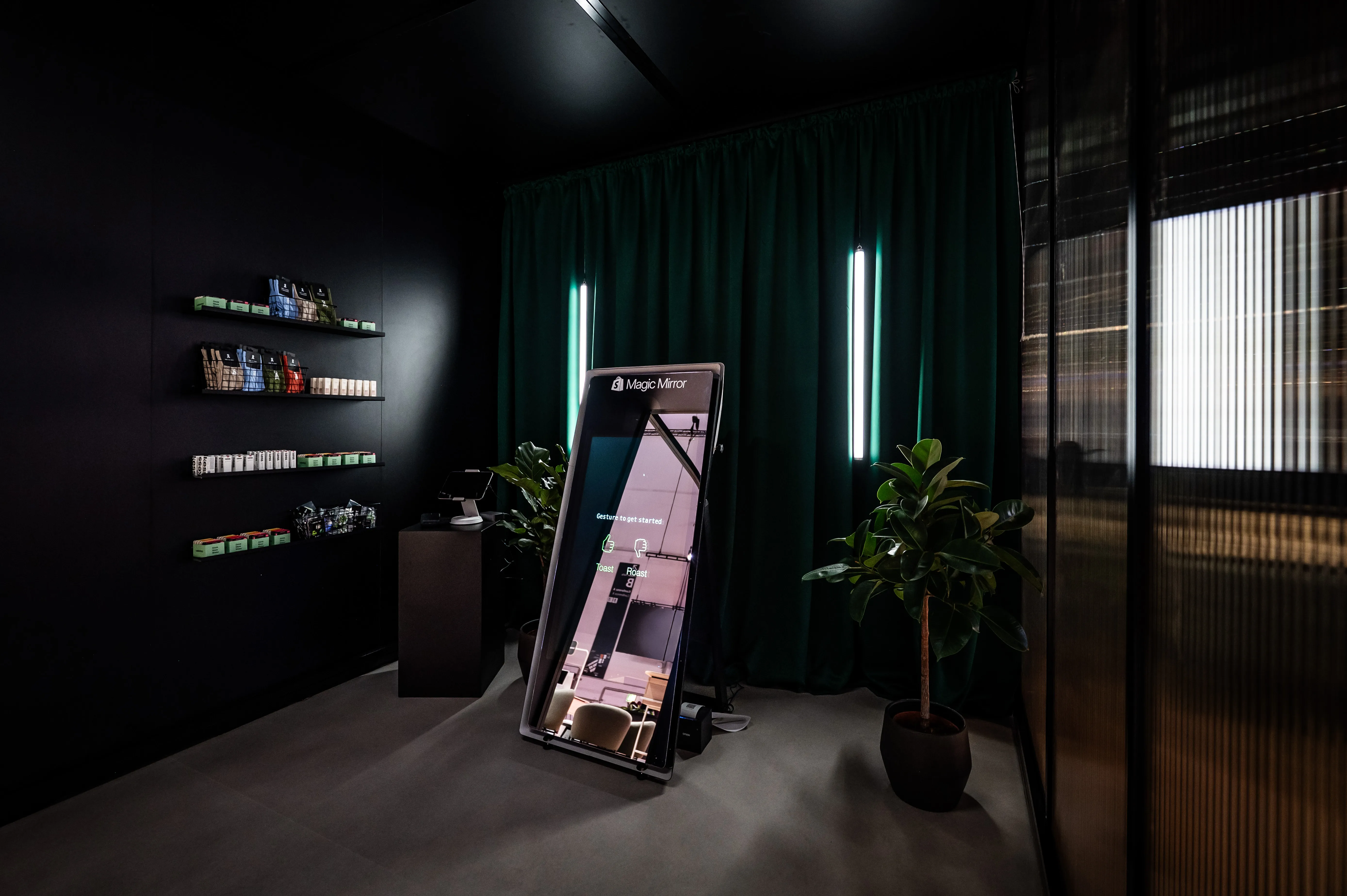 Magic Mirror photo station in a dark room with green curtain, plants and product shelves.