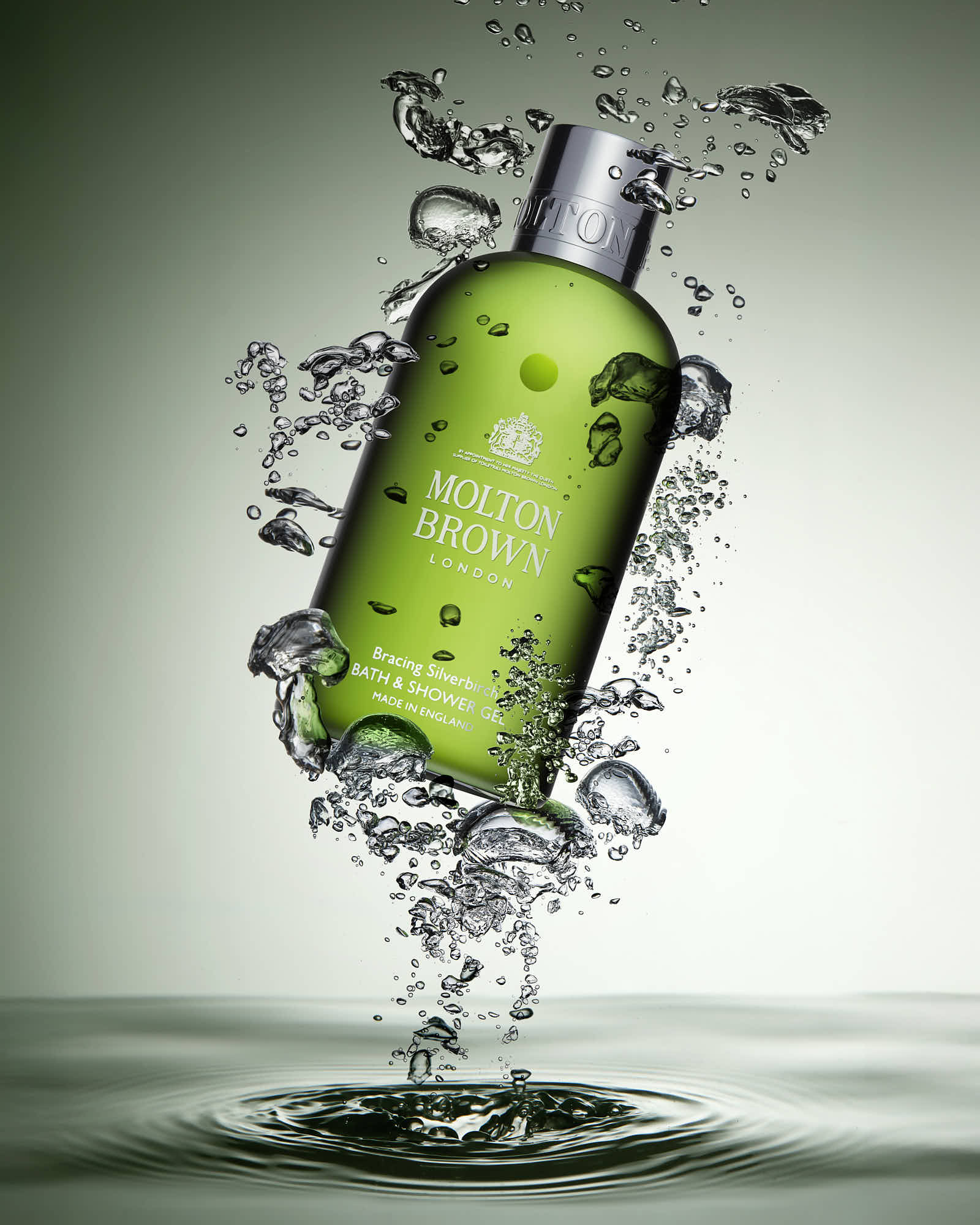 A green shampoo bottle surrounded by water droplets, against a soft gradient background.