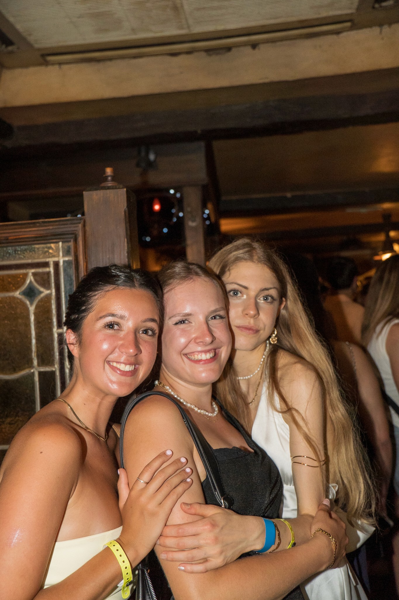 Three young women smiling and posing together inside a lively bar during a bar crawl in Nice capturing friendship shared energy and the social party atmosphere of nightlife on the French Riviera