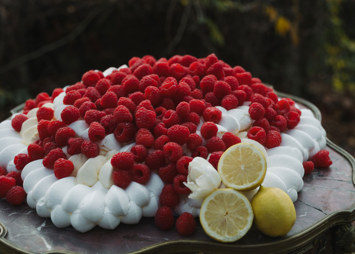 Modern buttercream wedding cake topped with fresh raspberries, piped cream and lemon accents in a refined editorial style