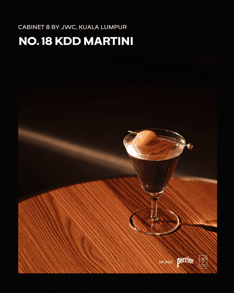 A KDD Martini served in a classic cocktail glass, featuring an olive garnish, on a wooden table with soft lighting.