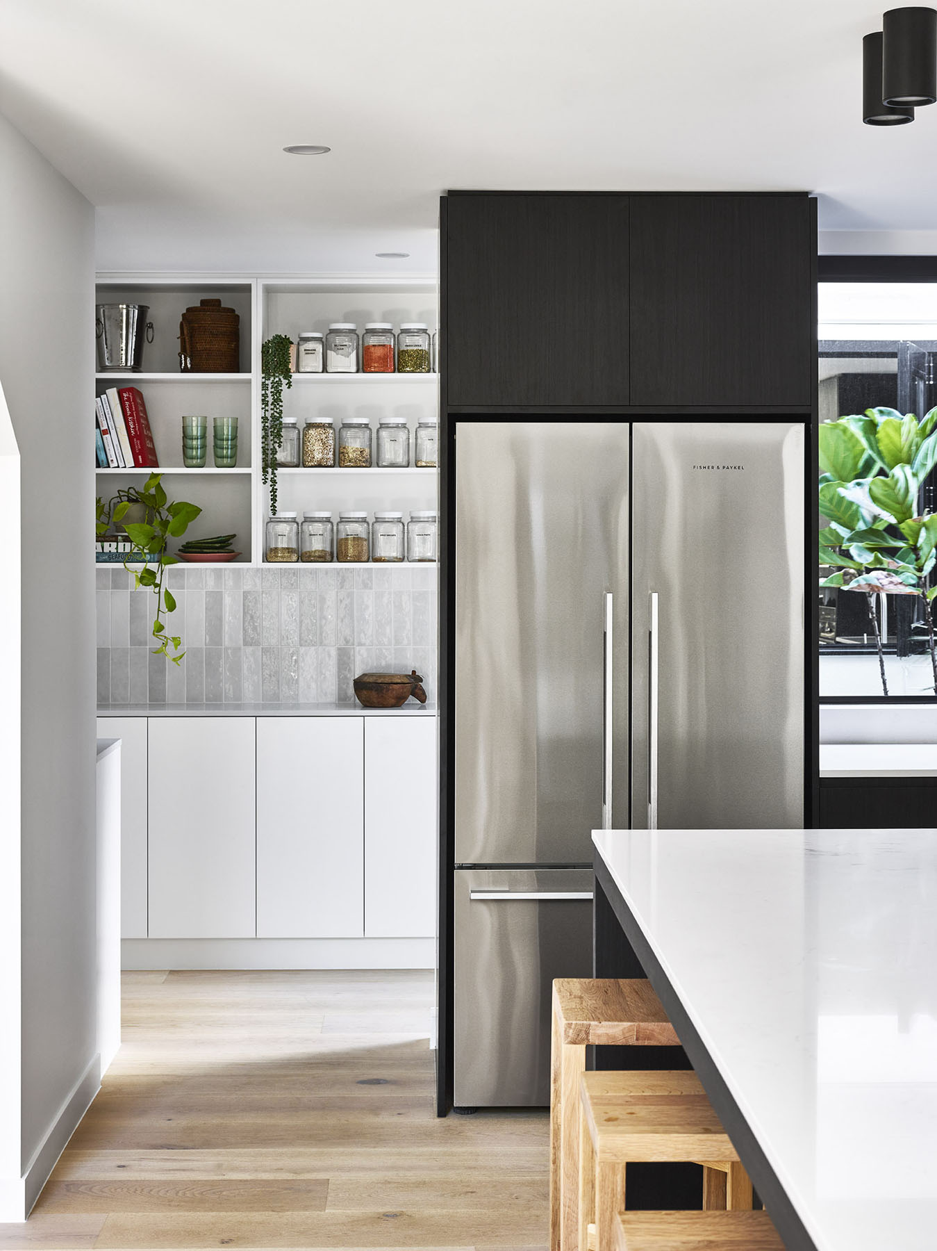 Kitchen detail with stainless steel fridge, open shelving, and tiled splashback.