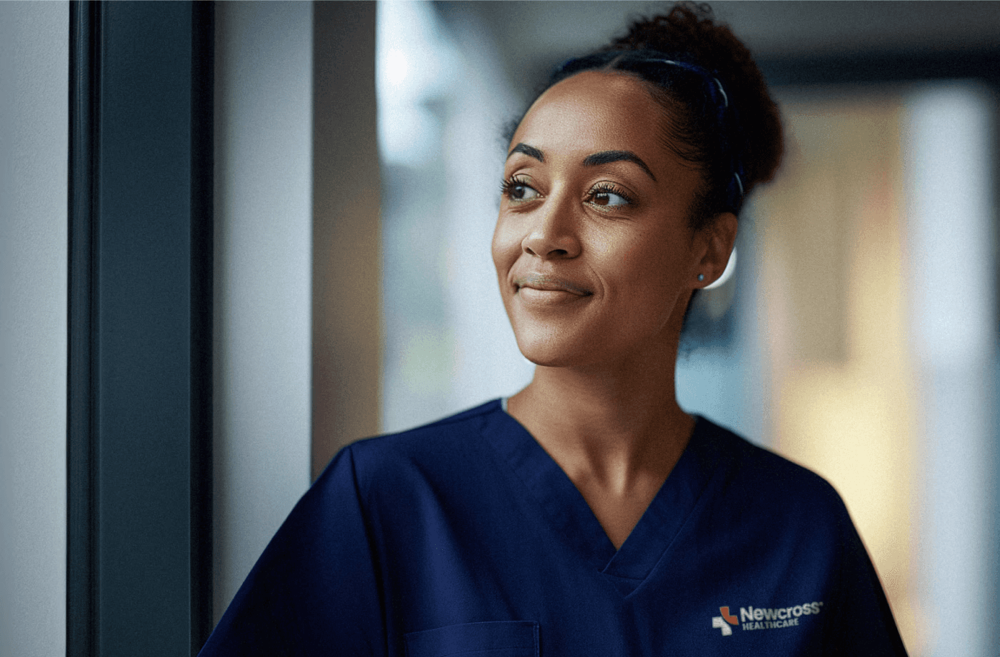 Healthcare professional wearing Newcross Healthcare navy scrubs looking upward with a thoughtful expression