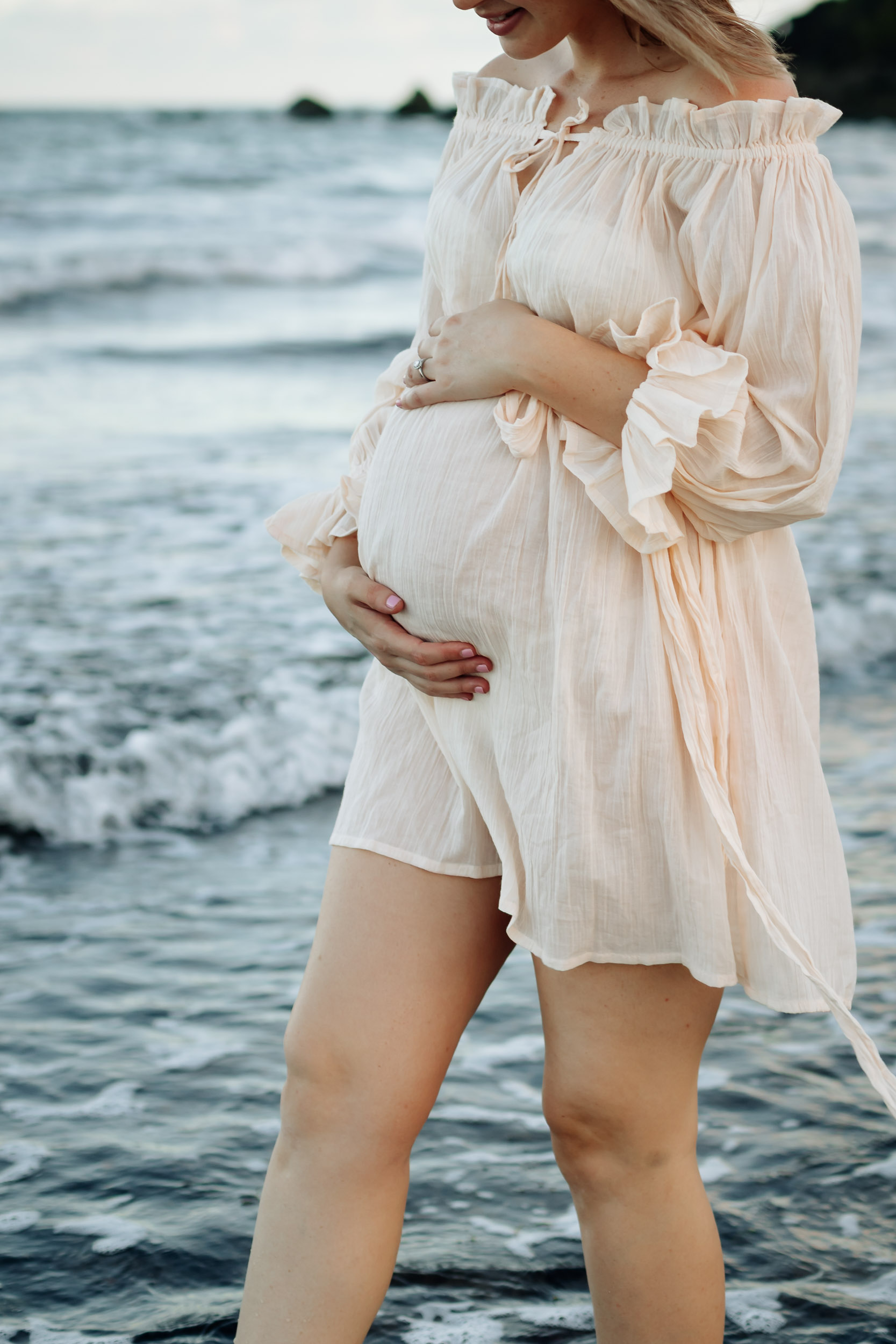 Golden hour maternity photo of expectant mother on the beach with soft waves and warm sunset light in Mackay Queensland.