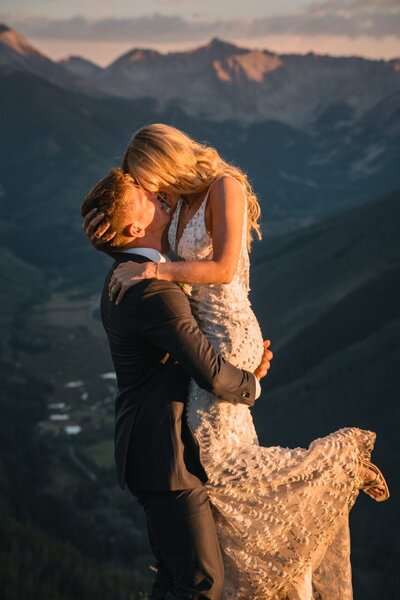 Tucker lifts Clemmie into his arms as they kiss against a mountain backdrop.