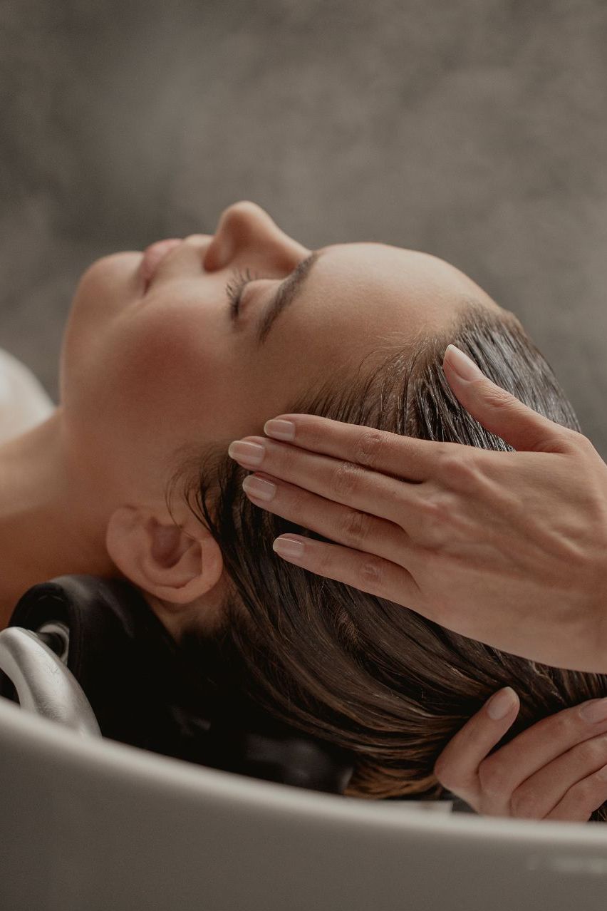 A woman lying down with a towel wrapped around her head, her face glistening with facial oil. Her eyes are closed, and she appears to be enjoying a spa treatment in a peaceful setting.