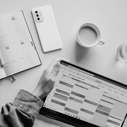 タブレットでカレンダーを確認しながら日程調整を行う様子。スマホと手帳、コーヒーが置かれたデスク