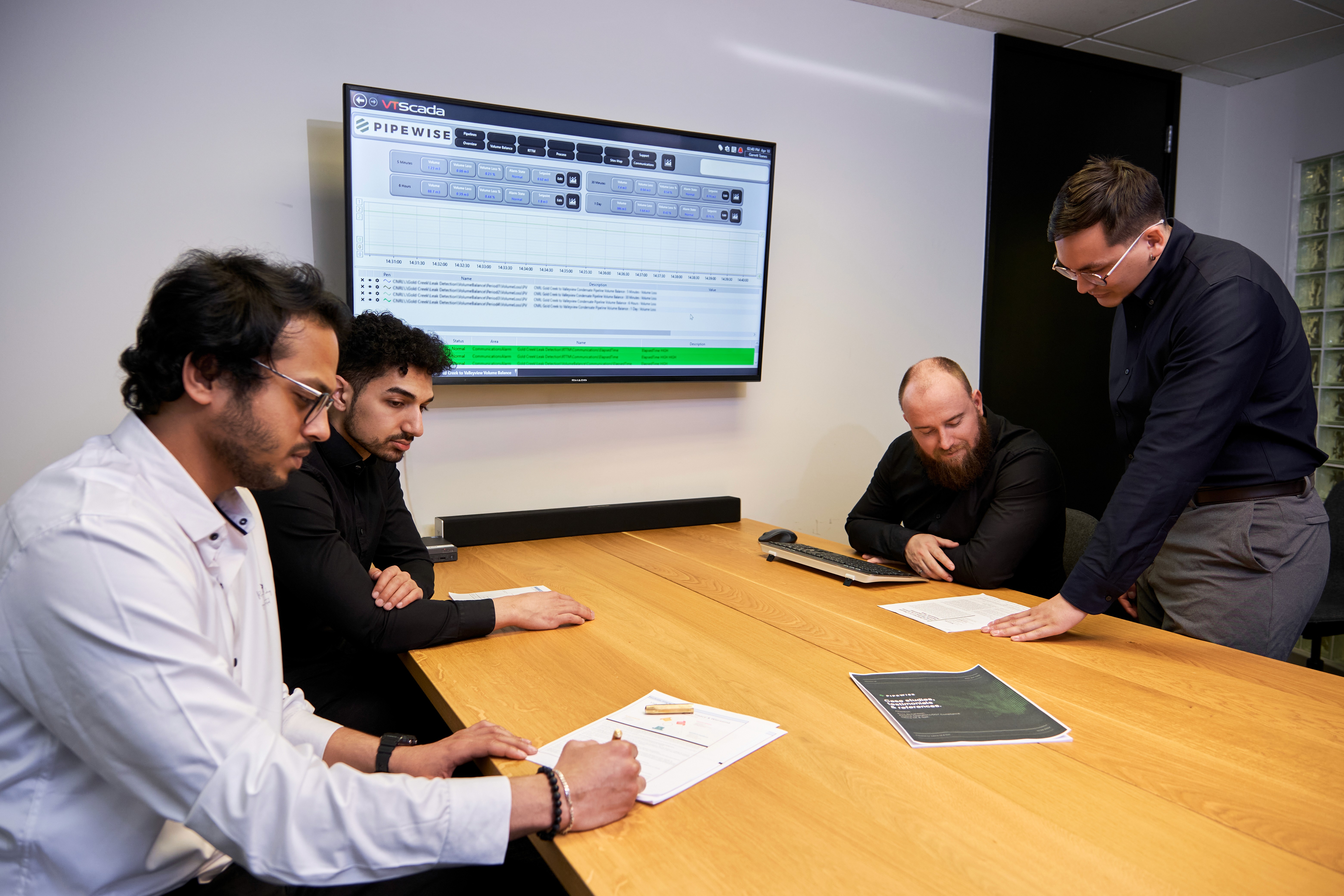 Four diverse professionals collaboratively working on a laptop, with one person pointing at the screen while others observe.