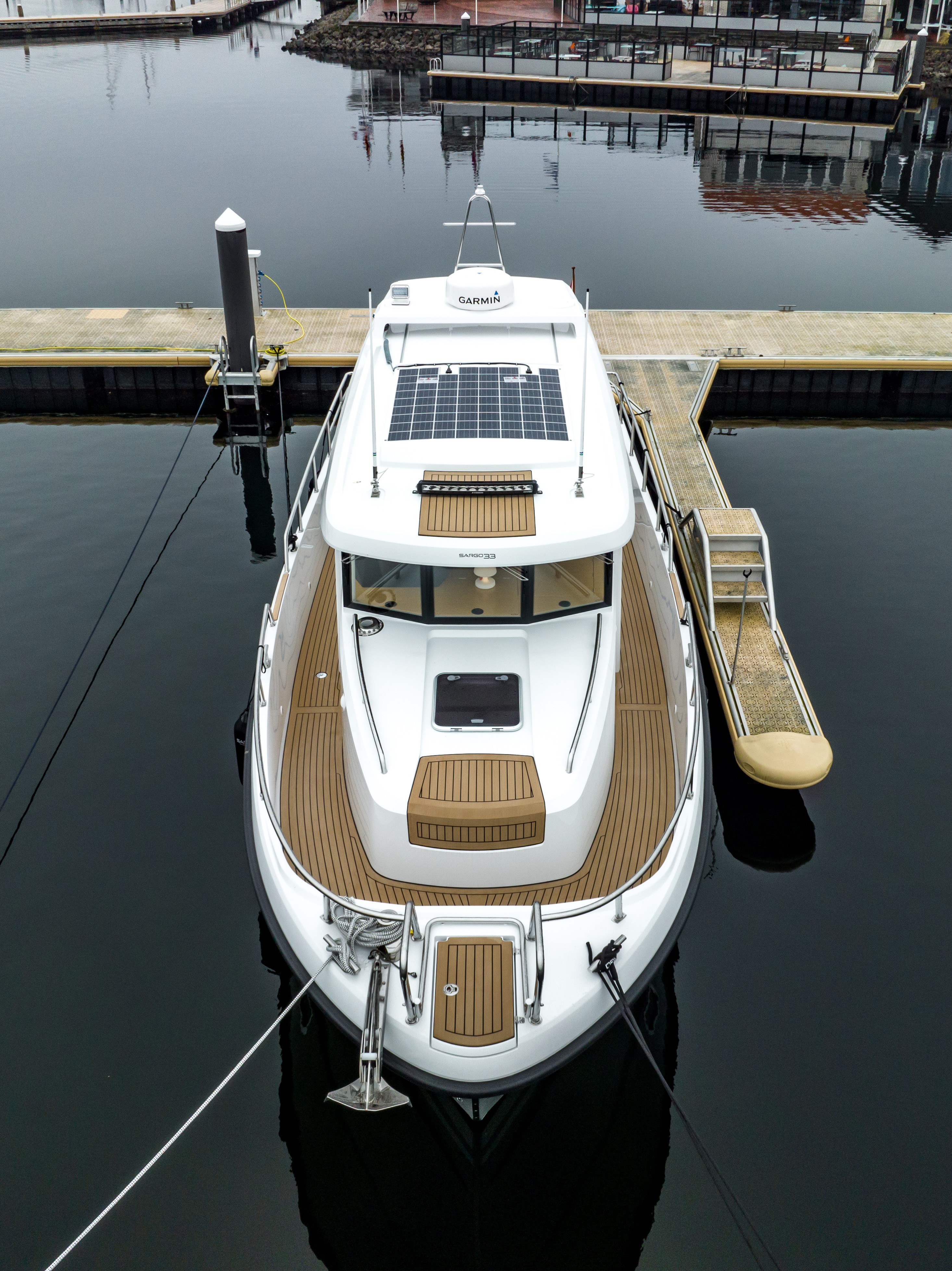 Aerial overhead view of a motor yacht moored at a marina pontoon, showcasing a full EcoDeck composite deck installation in light oak across the entire deck surface, cockpit, and hardtop roof, demonstrating seamless full-vessel deck coverage