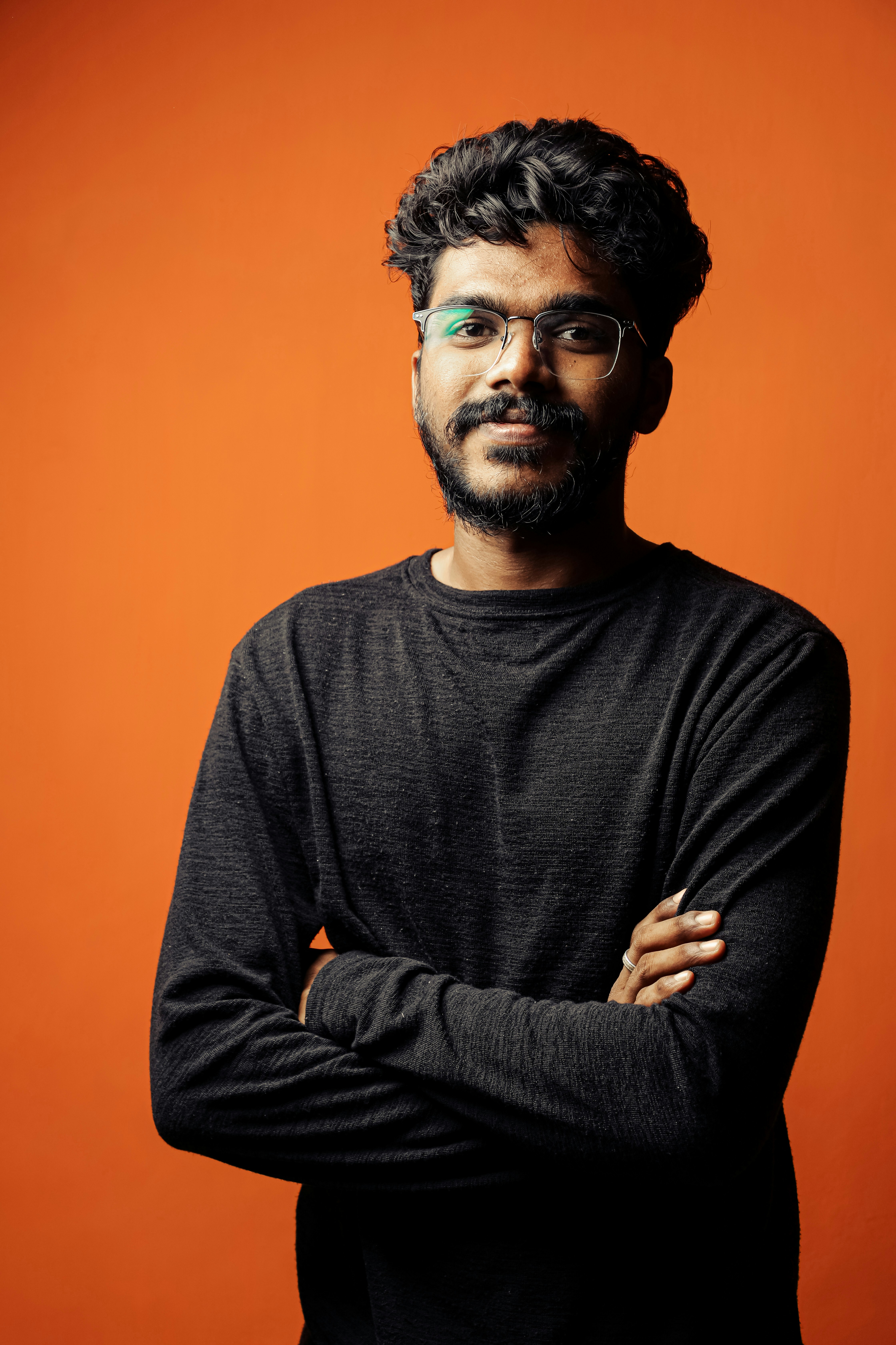 a man with a beard and glasses standing with his arms crossed