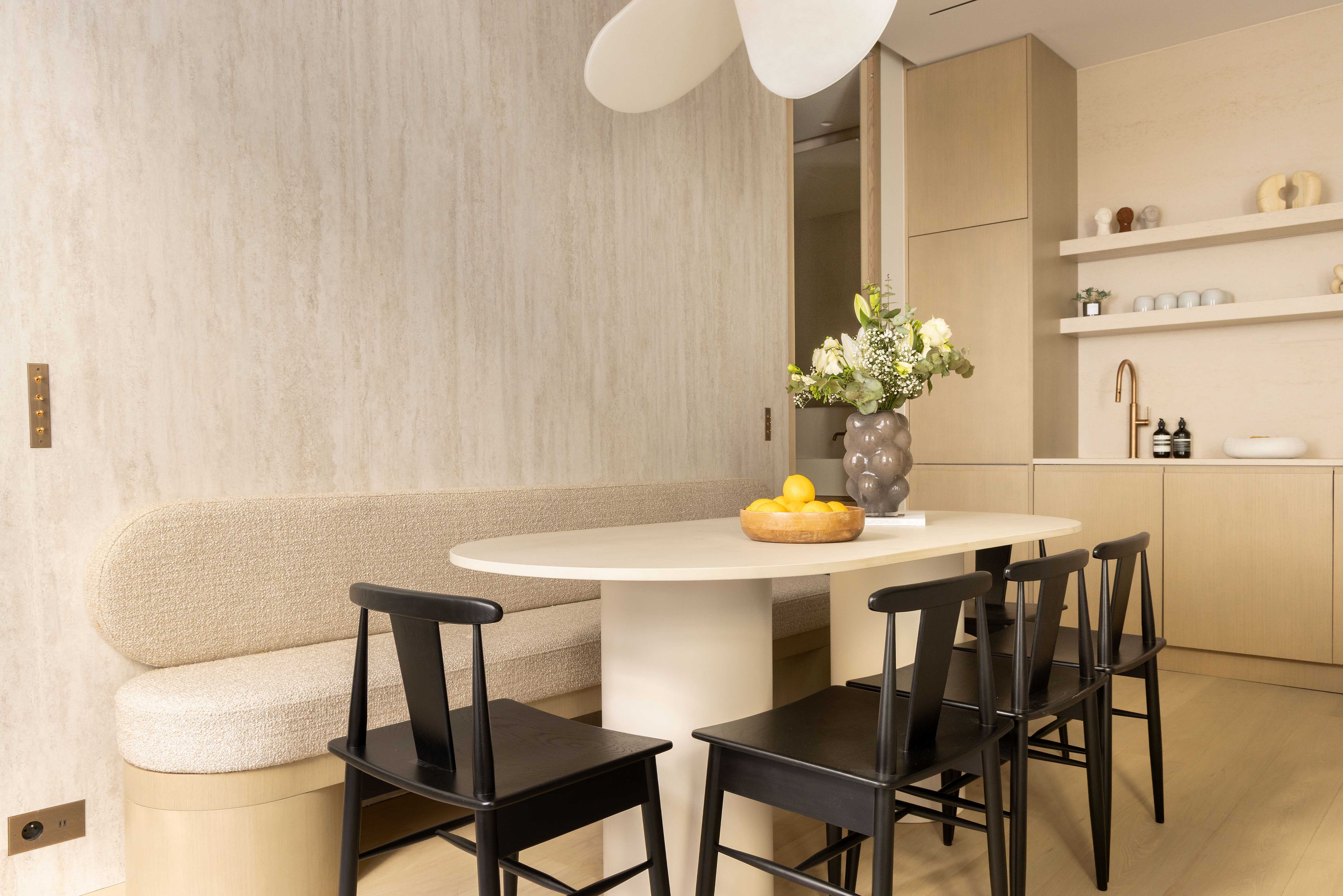 Salle à manger vue depuis le salon avec banquette, chaises noires et cuisine en arrière-plan