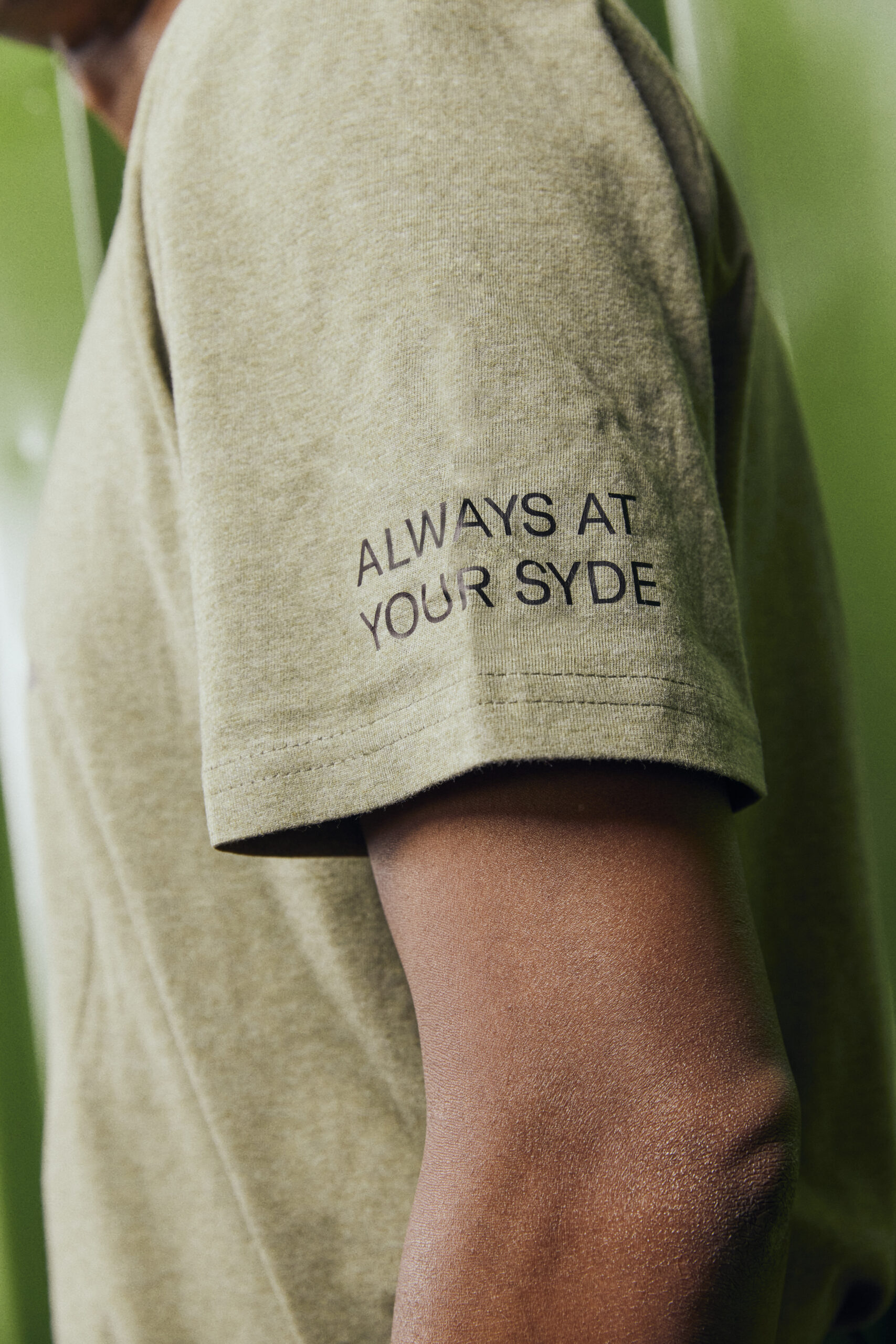 Smiling young woman with long hair standing against a dark green background, holding a finger to her chin.
