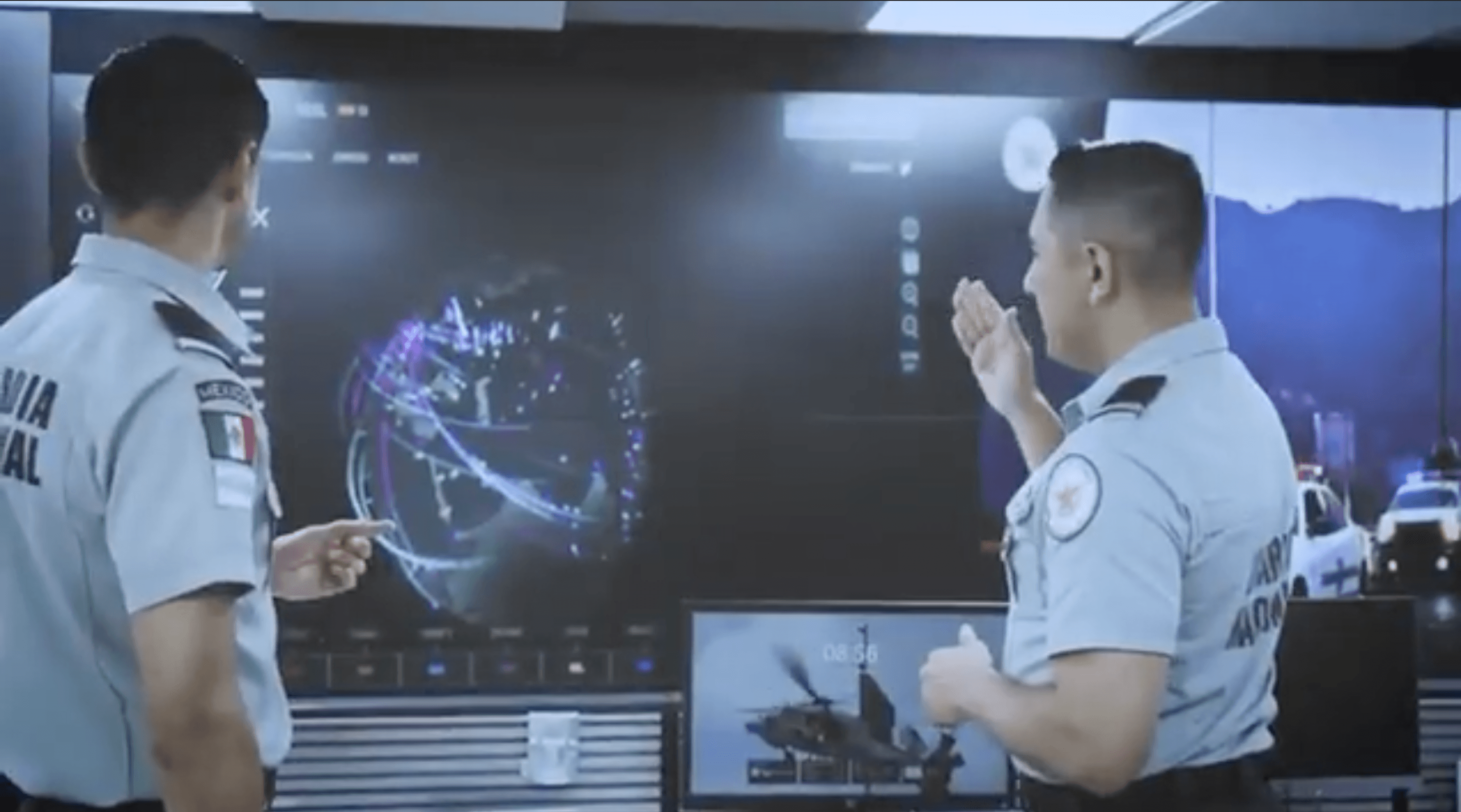 **Alt text:** *Two security personnel monitor and discuss data displayed on a large digital command-center screen.*
