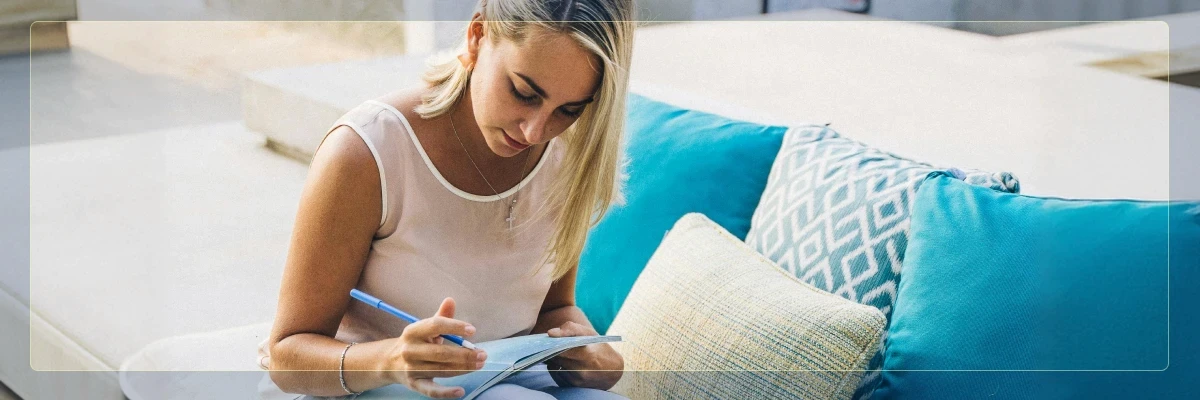 A woman relaxing on a couch outdoors and writing calmly in a notebook.