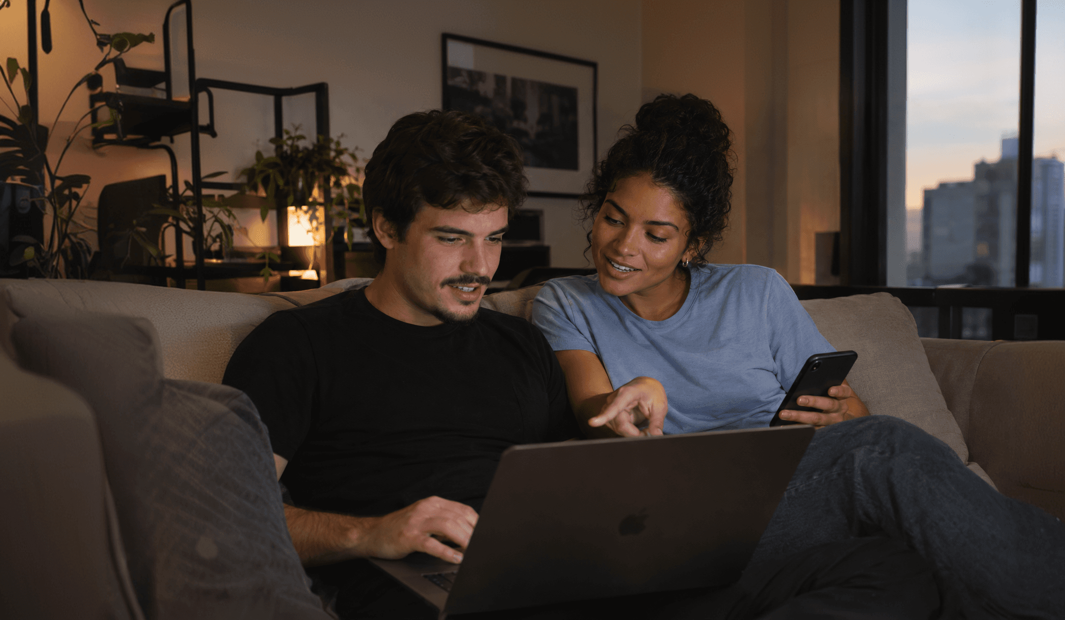 Casal no sofá olhando o celular e o notebook