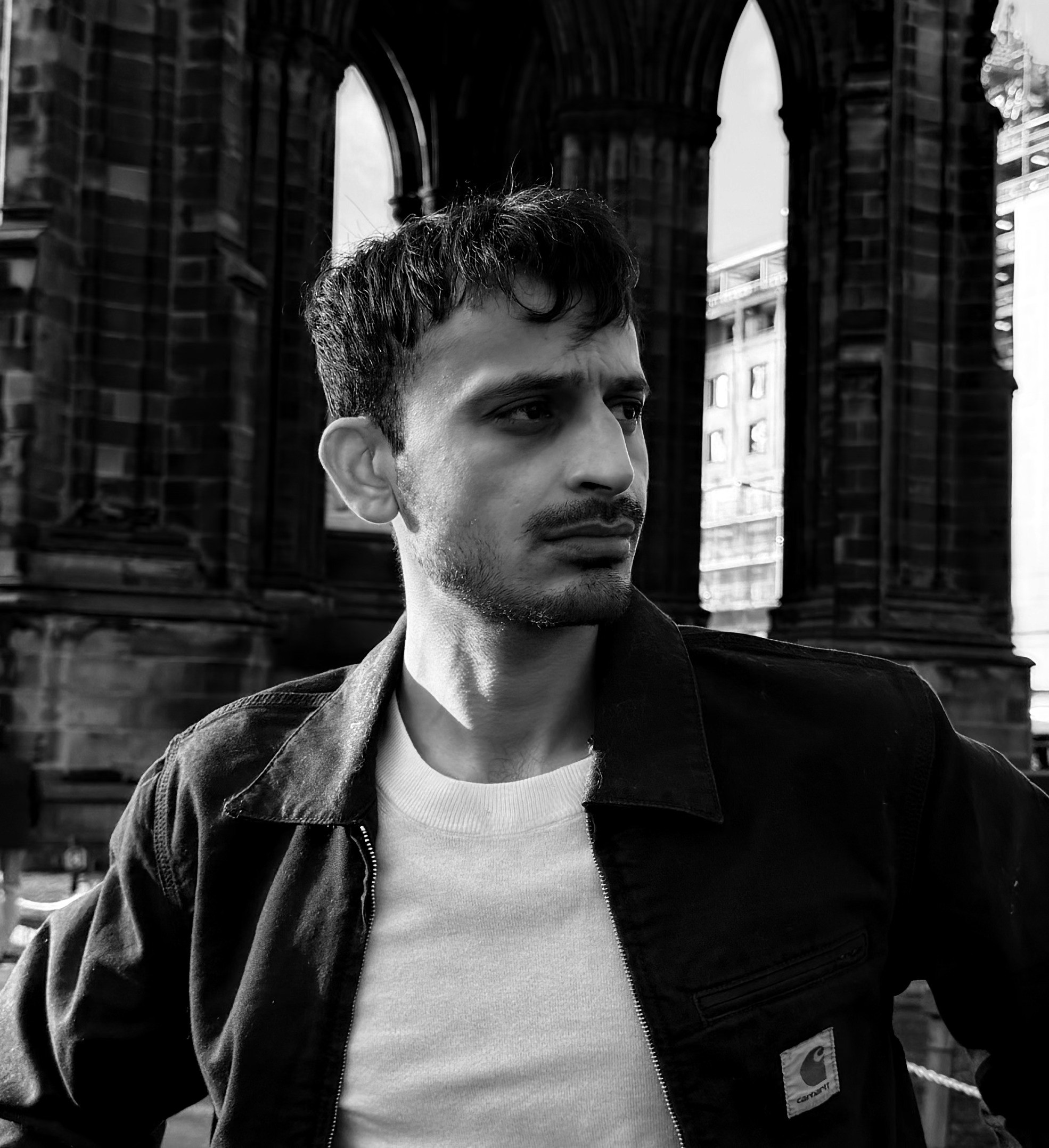 A thoughtful young person with dark hair gazes to the side, captured in soft black and white lighting.