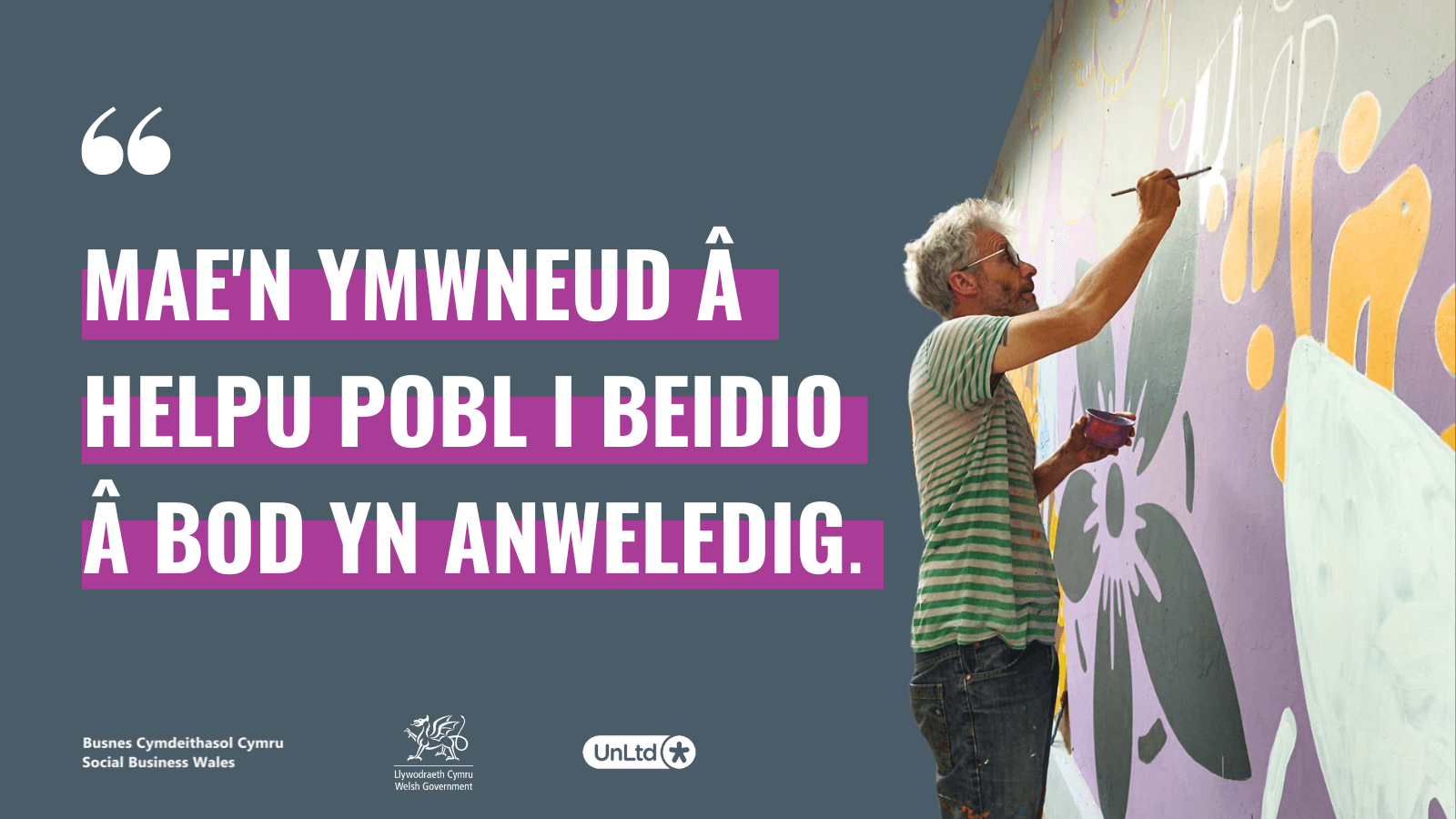 A man painting a mural on a wall with a graphic of a quote in Welsh highlighted in purple.