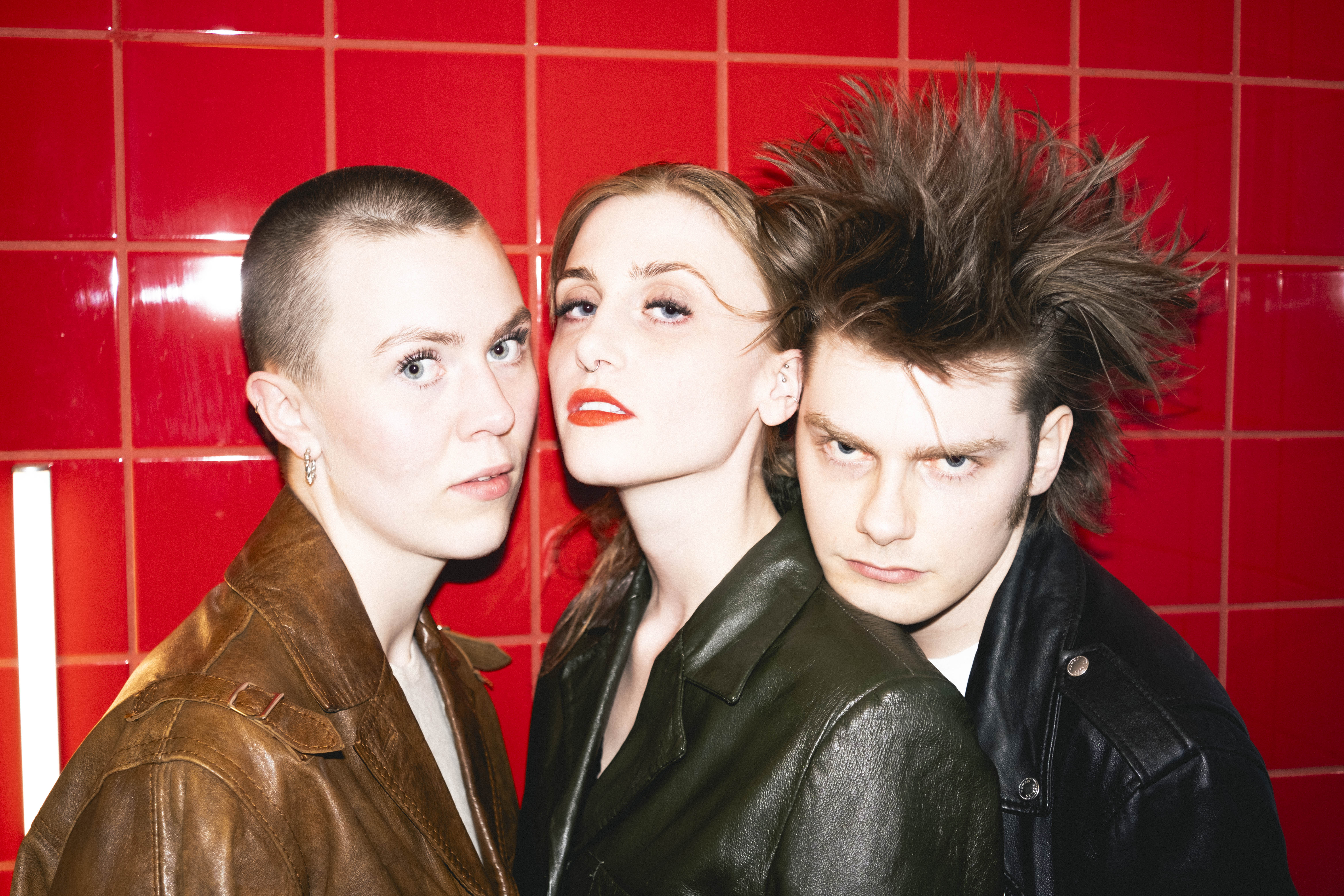 A close-up portrait of the three members of the Icelandic band virgin orchestra posing against a bright red tiled wall. Photograph by Kaja Sigvalda.