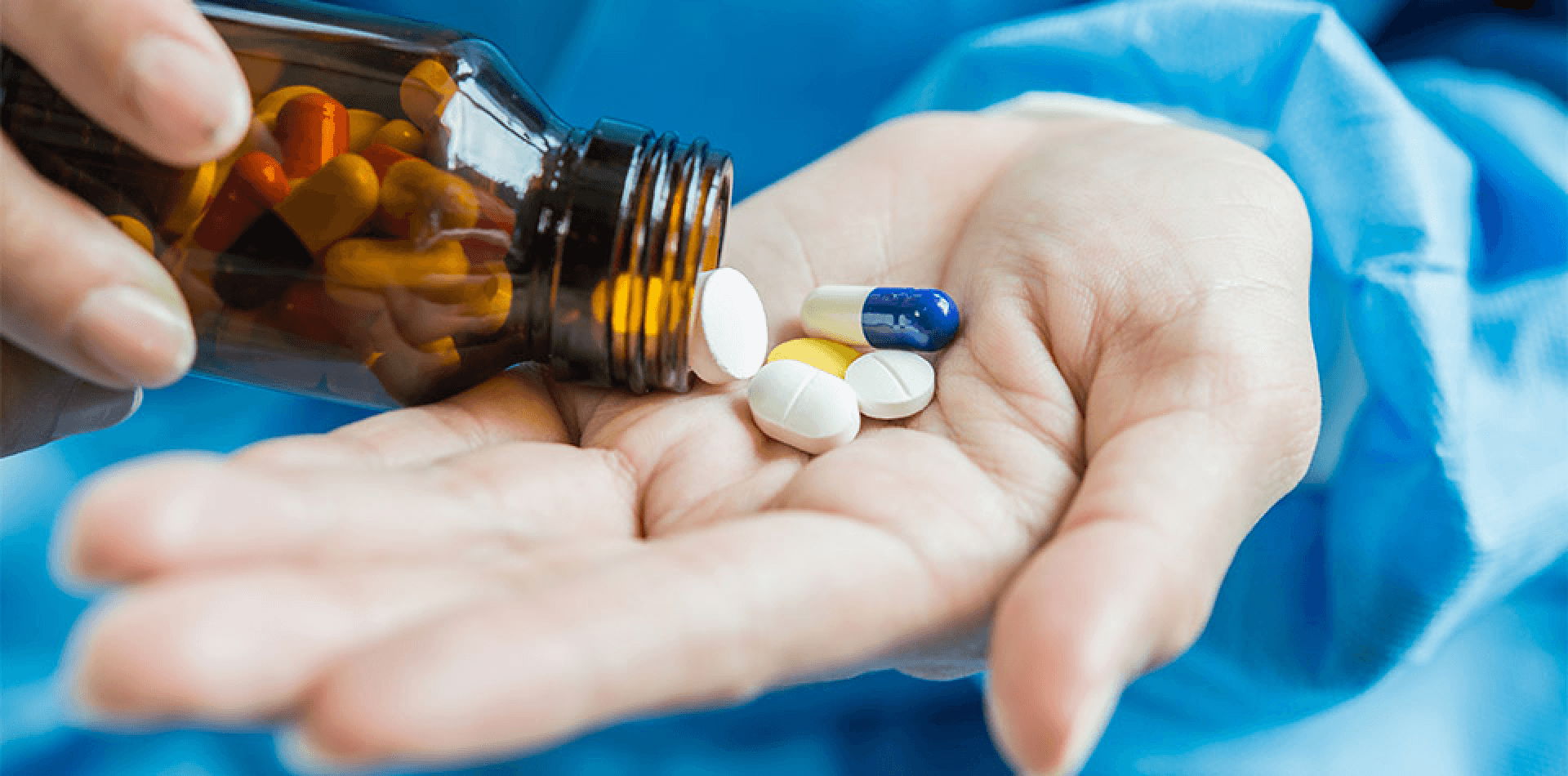 Various pharmaceutical pills and capsules in a healthcare worker's hand.