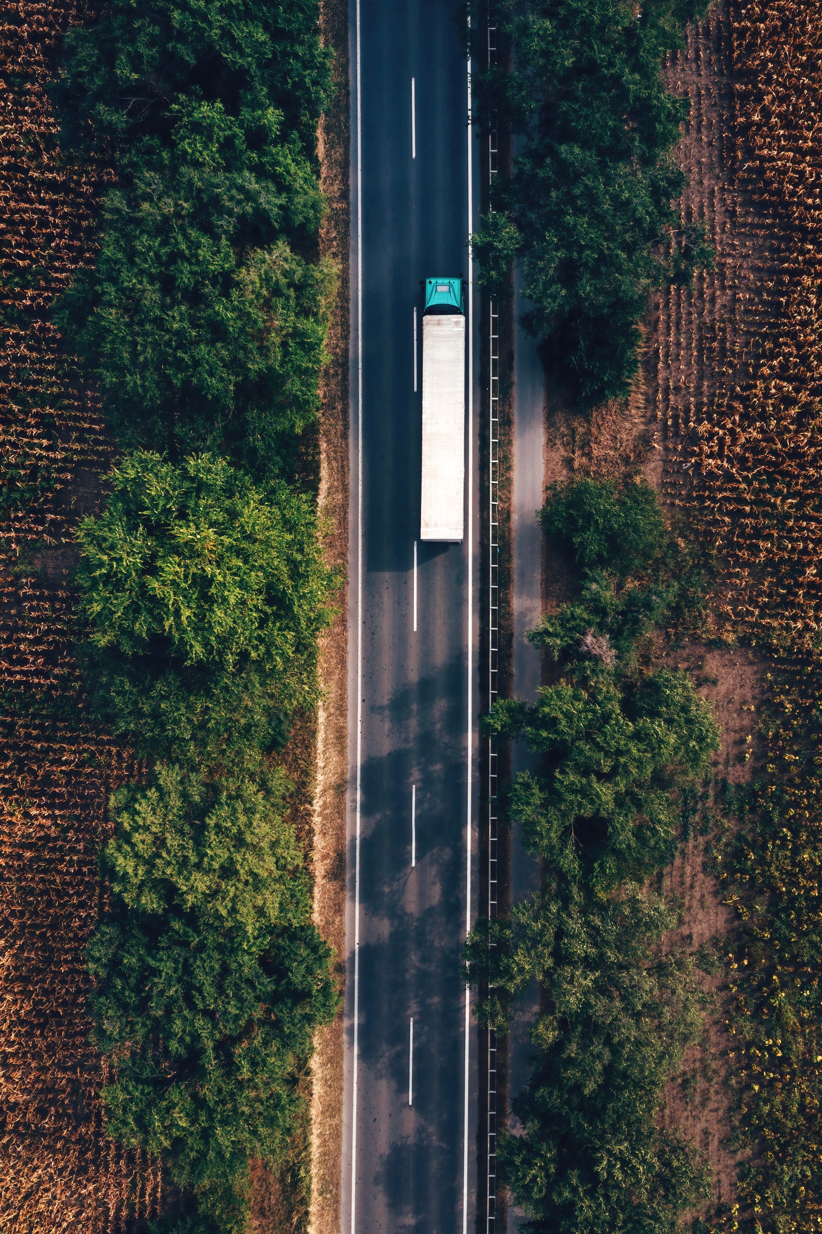 Aerial view of a semi-truck driving on a rural road flanked by trees and farmland