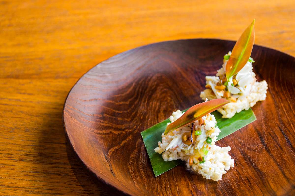 A wooden plate holds two mounds of sushi rice topped with green onions and garnished with a thin slice of orange.