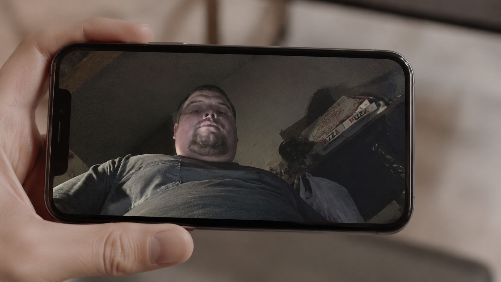A close-up view of a hand holding a smartphone displaying a video call of a man