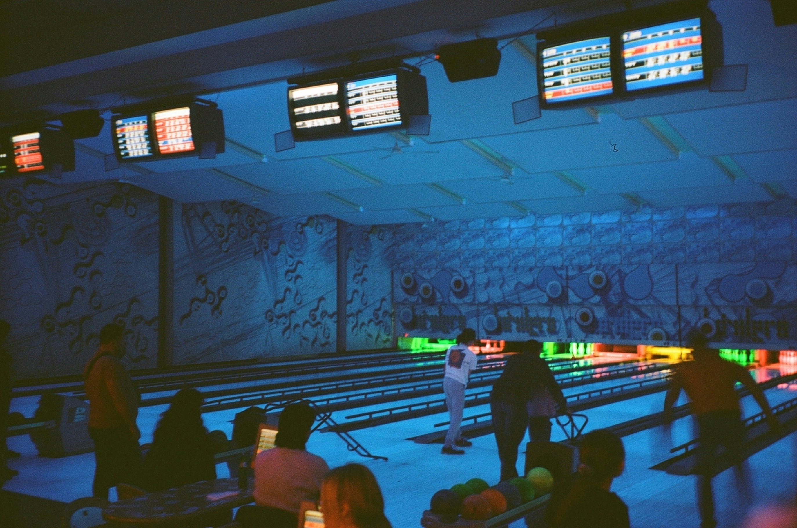 Bowlers silhouetted under blue light in a dark bowling alley