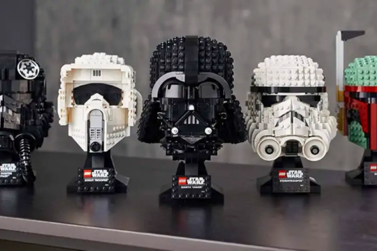 A collection of LEGO Star Wars helmet sets displayed on a shelf, featuring Darth Vader, a Stormtrooper, a Scout Trooper, a TIE Fighter Pilot, and Boba Fett, each intricately built for display.