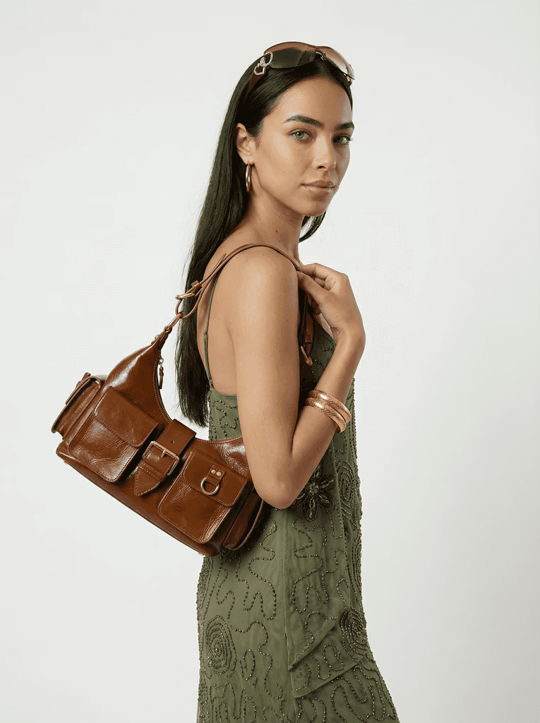 A person wearing a plain white t-shirt and a black cap stands against a neutral gray background, looking directly at the camera, with their hands relaxed by their sides.
