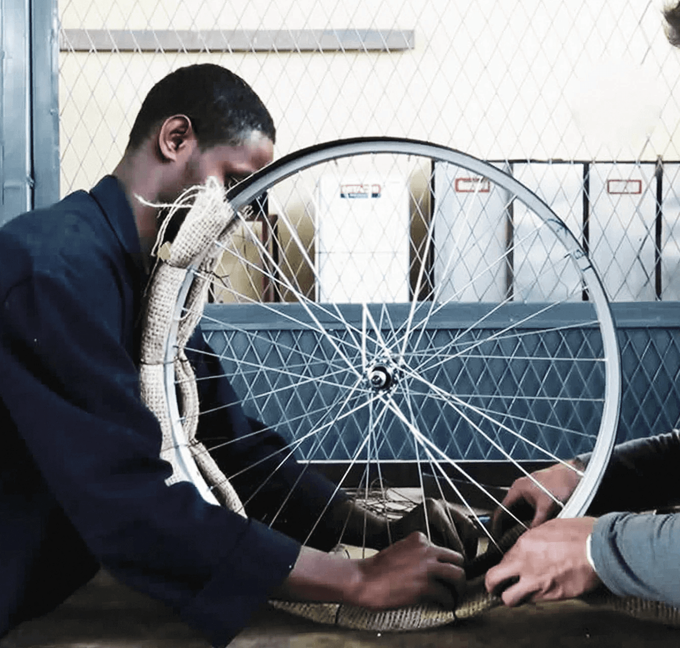 Two people connecting burlap to bicycle wheel.