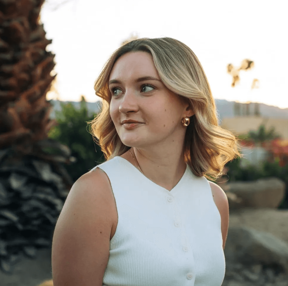 Woman in white top looking left, outdoors at sunset