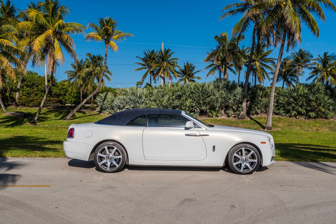 Side profile of the Rolls-Royce Dawn convertible, showcasing its elegant design against a tropical landscape.