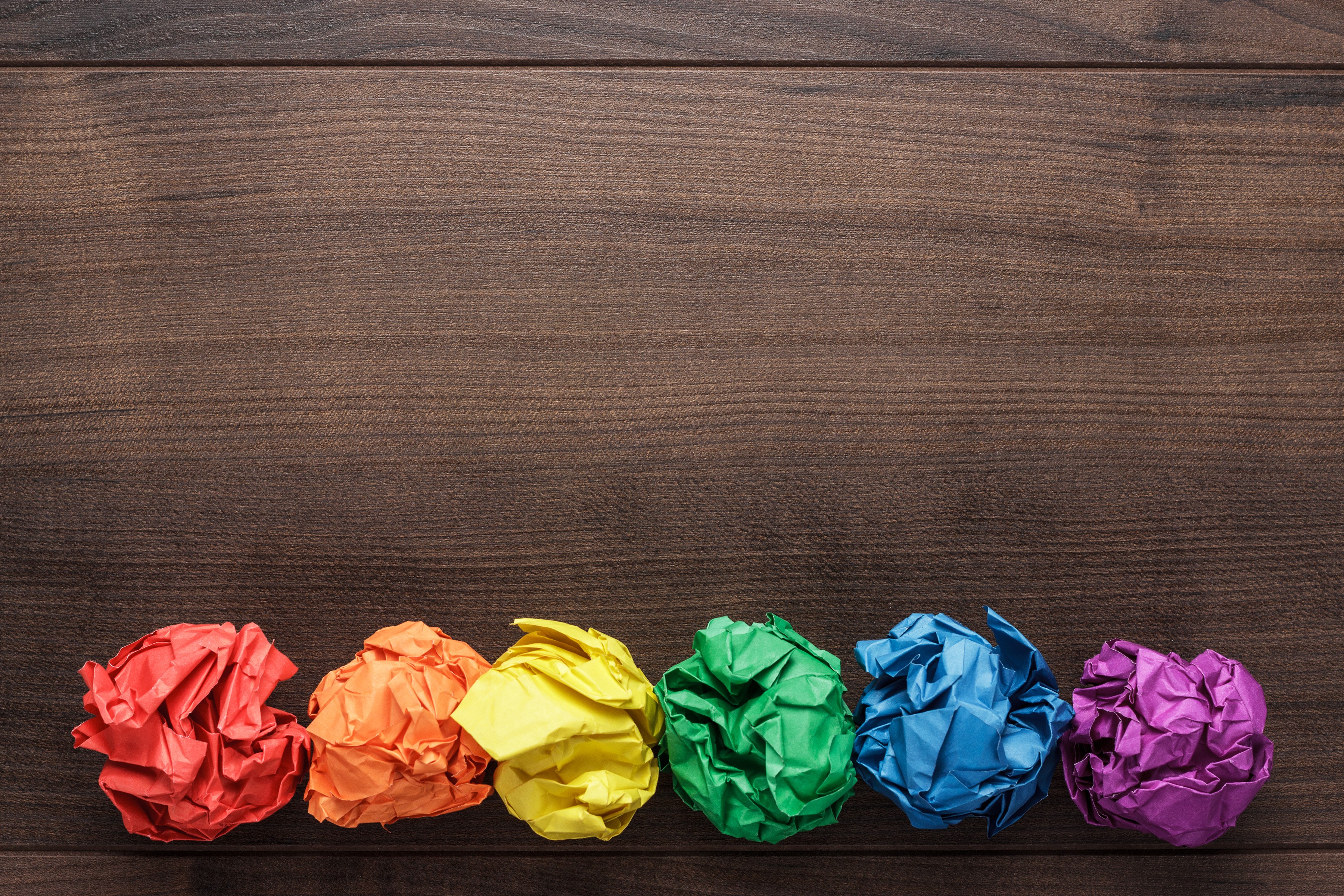 Six crumpled paper balls in rainbow colors lined up on a wooden desk background