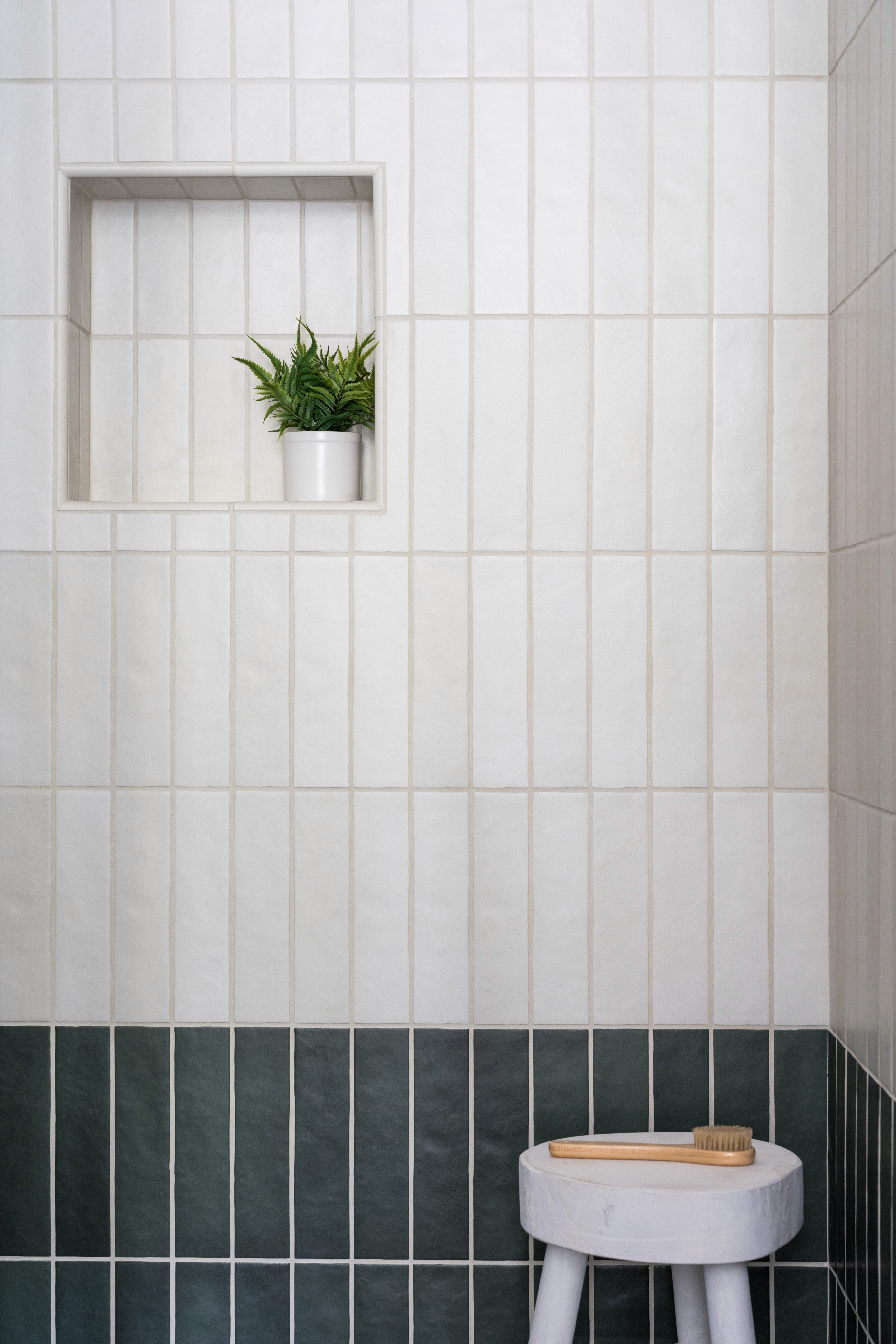 Guest showers with off-white tile on top two-thirds of wall and dark blue-grey tile on bottom third and a modern, white shower stool by Jubilee Interiors in Arcadia, California