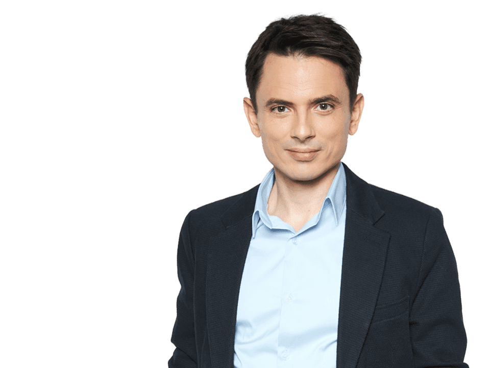 A person wearing a blue dress shirt and dark blazer stands confidently against a plain background, embodying a professional and polished appearance.