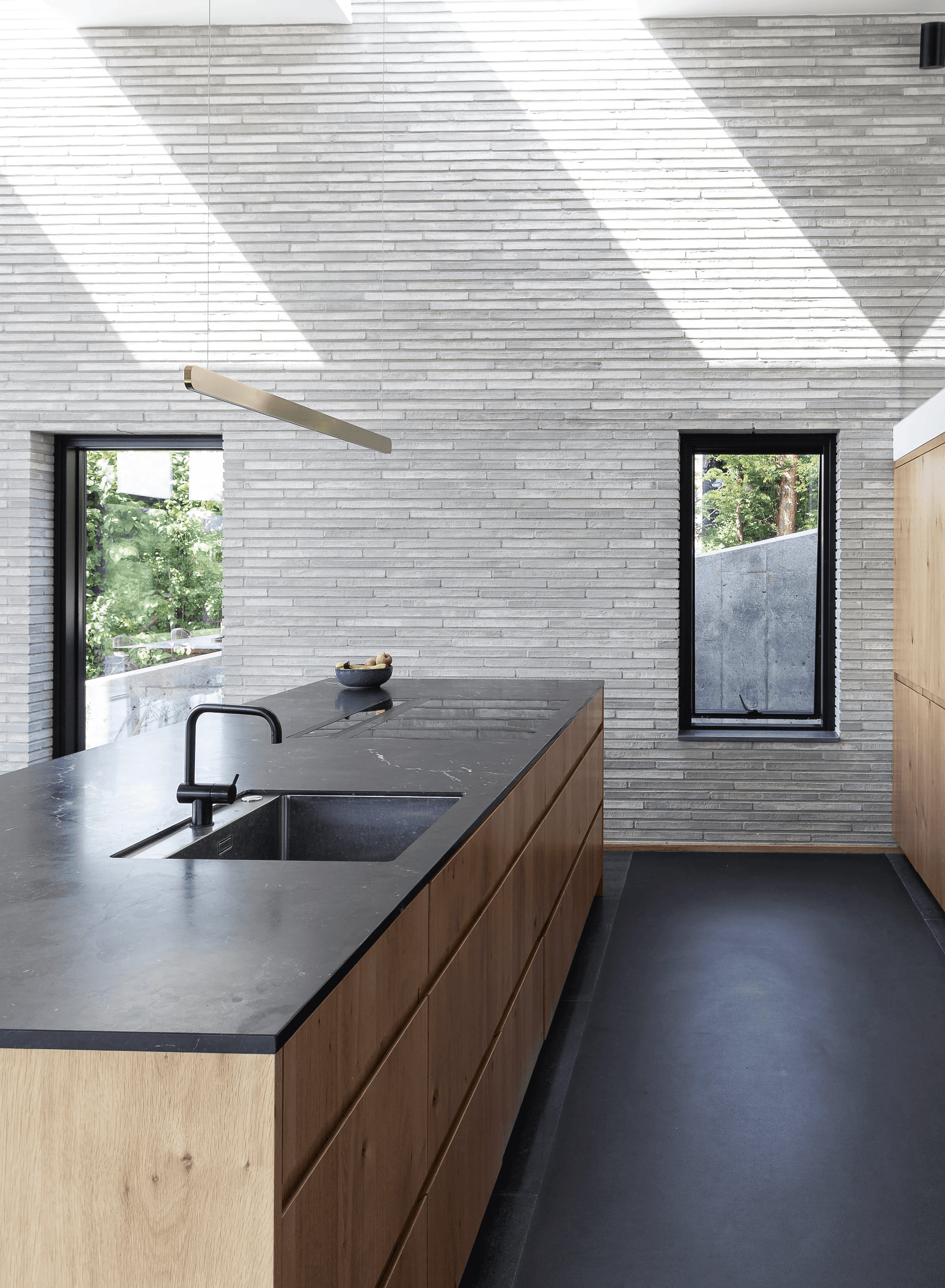 En moderne bygning i glas og mursten ved en sø, omgivet af frodigt grønt græs og en stensti. Himlen er overskyet, hvilket skaber en rolig og fredfyldt atmosfære.