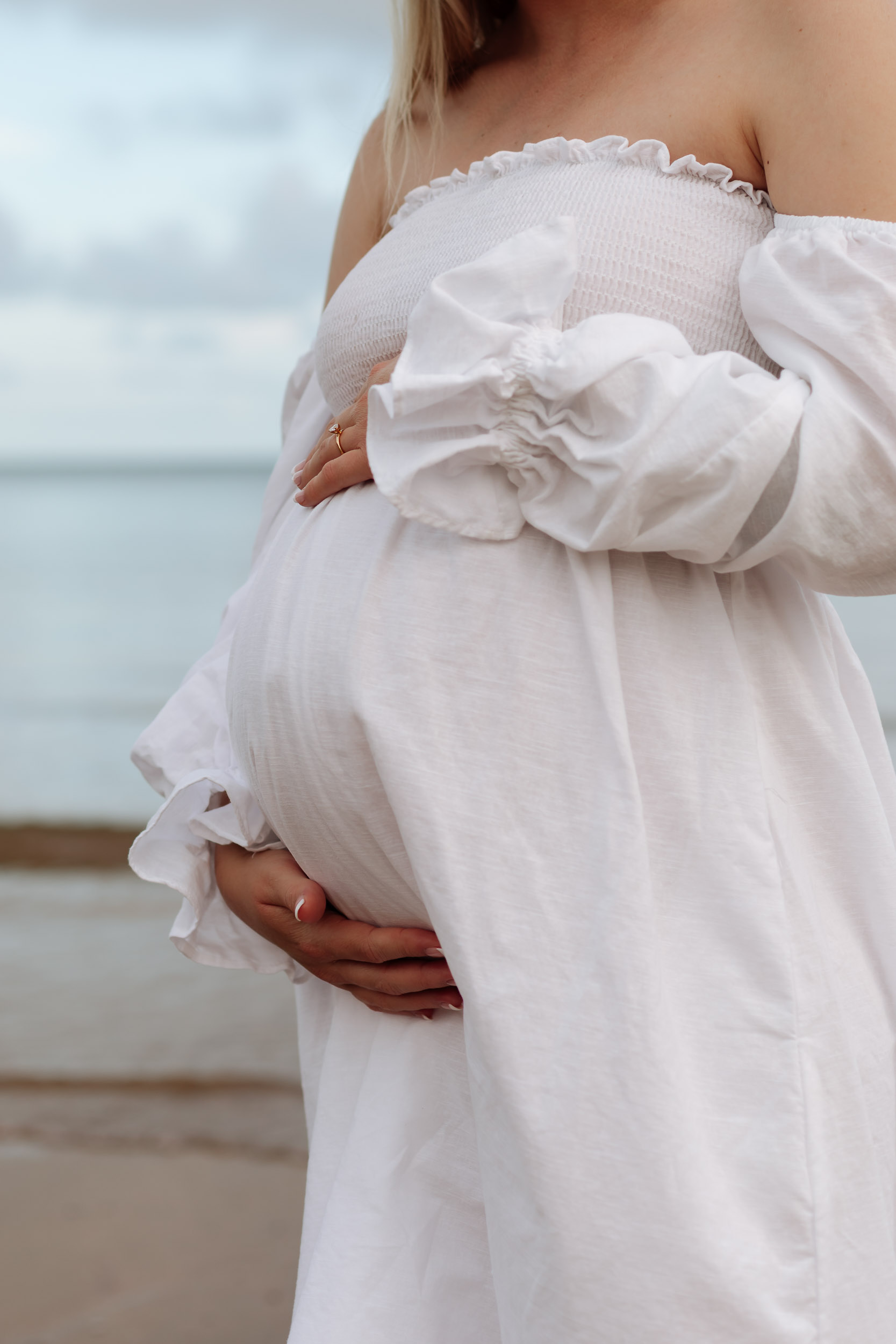 Pregnant mother standing alone on the shoreline at golden hour with soft sunset light over the ocean in Mackay