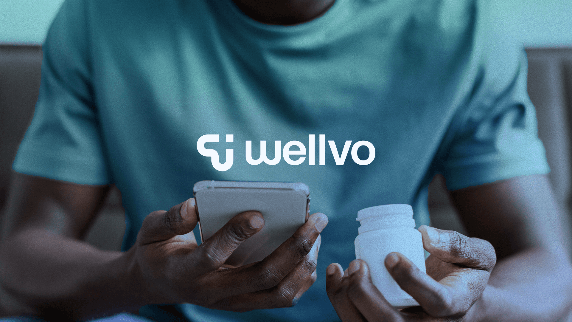 A person in a green shirt and jeans holding a smartphone and a pill bottle.