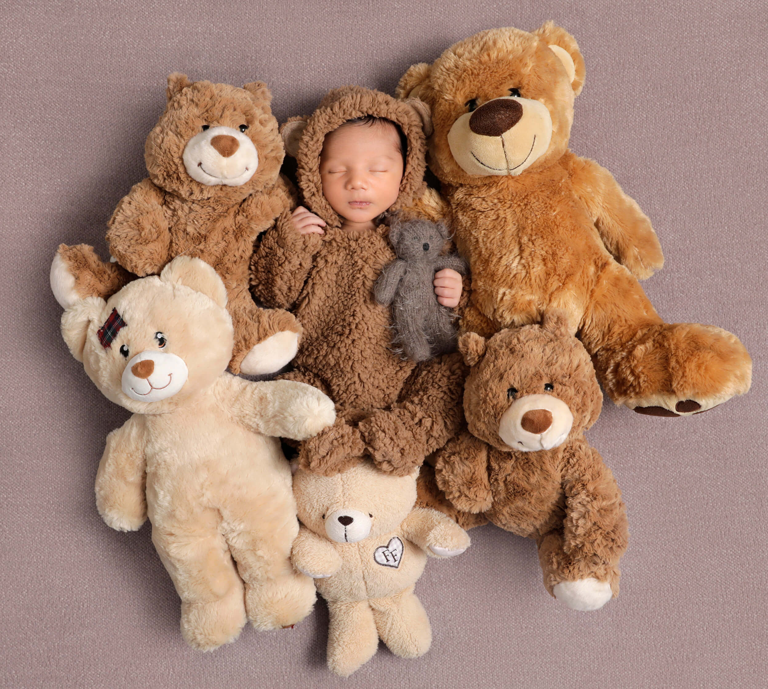 A newborn baby with stuffed bears as a concept for how to become a newborn photographer