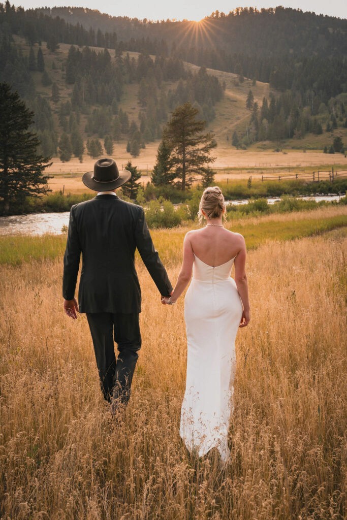 Newlyweds walking away through a mountain meadow