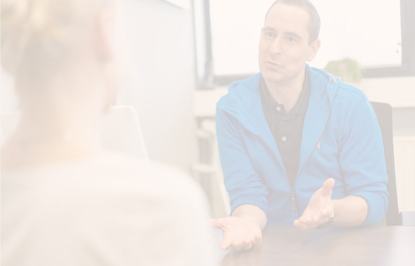 A group of four people, two men and two women, stand together smiling in a bright, modern office hallway, dressed in casual professional attire.