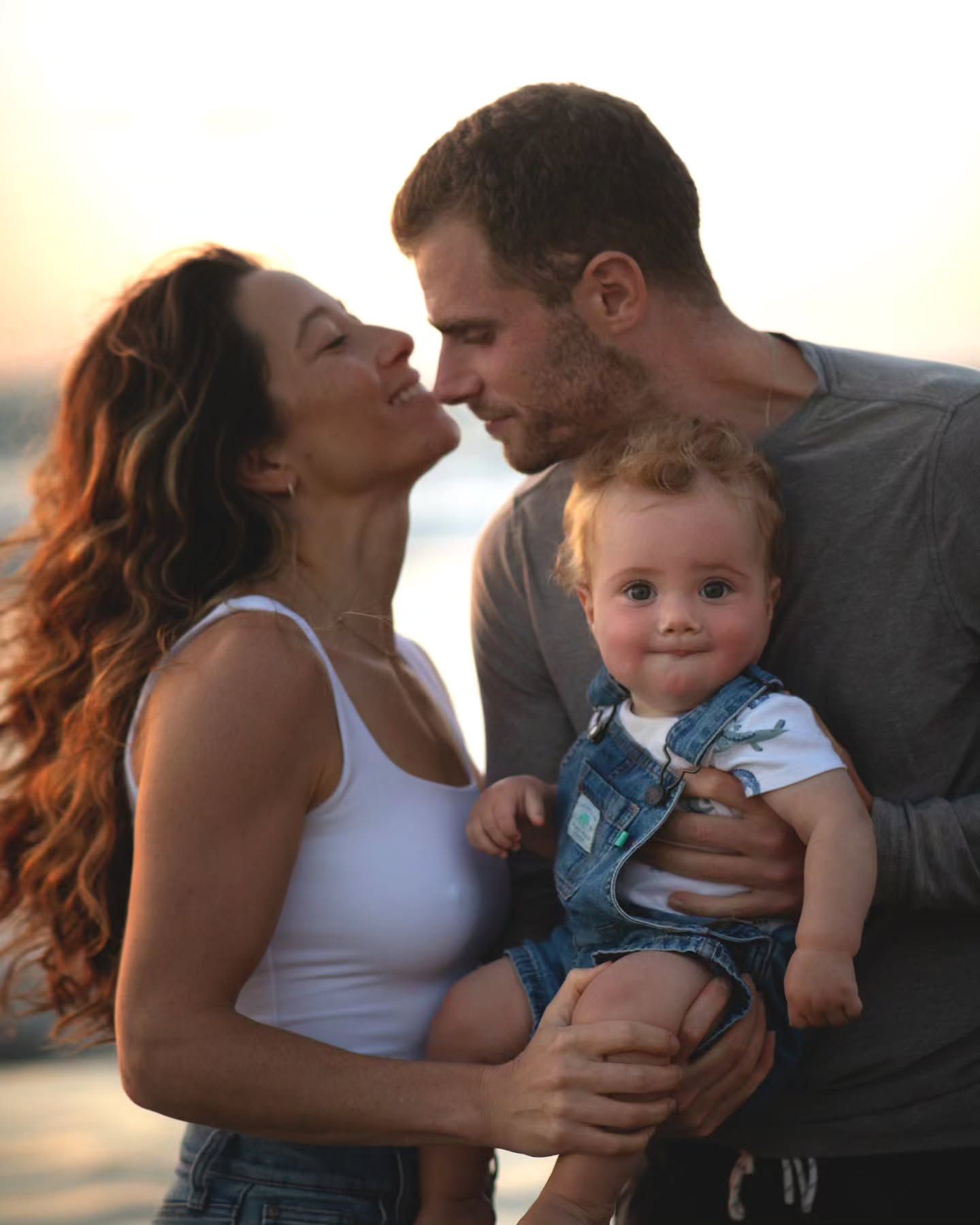 Parents holding their toddler in warm evening light during a relaxed family photoshoot.