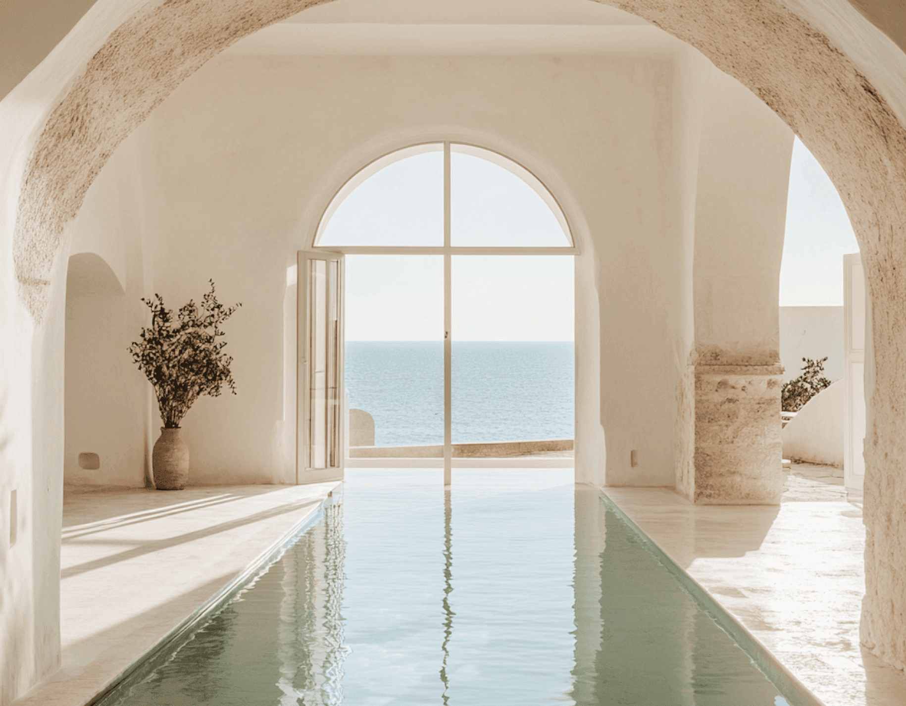 Elegant indoor pool with arched stone walls and ocean view through large window.